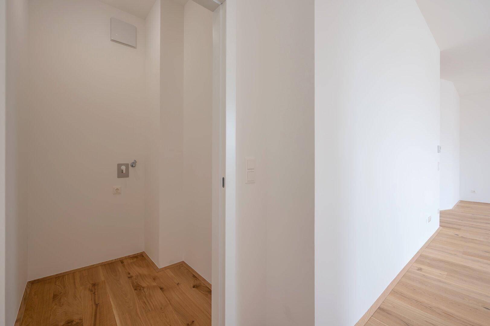 Praktischer Hauswirtschaftsraum mit Anschlüssen für Waschmaschine und Trockner, ausgestattet mit Holzboden.