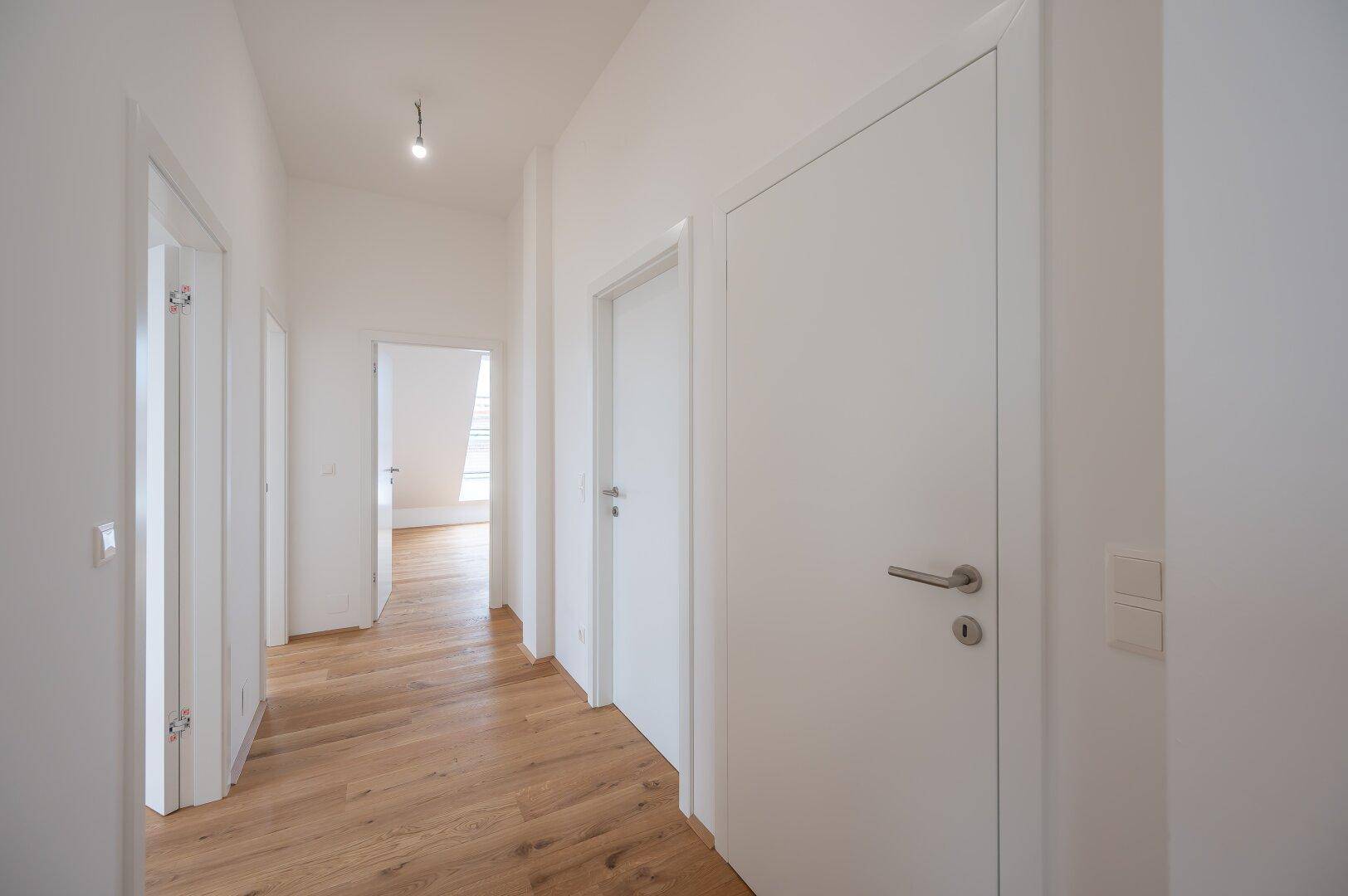 Langer, heller Flur mit Holzboden und mehreren weißen Türen, die zu den angrenzenden Zimmern führen.