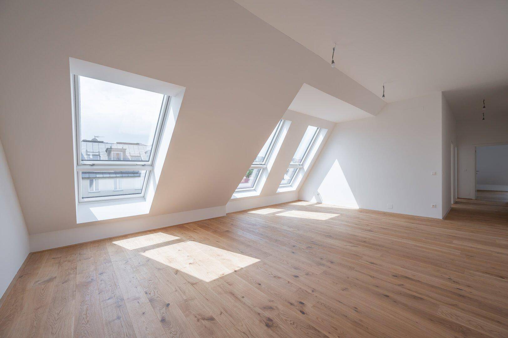 Geräumiger Dachgeschossraum mit hellem Holzboden und mehreren Dachfenstern, die den Raum mit Licht füllen.