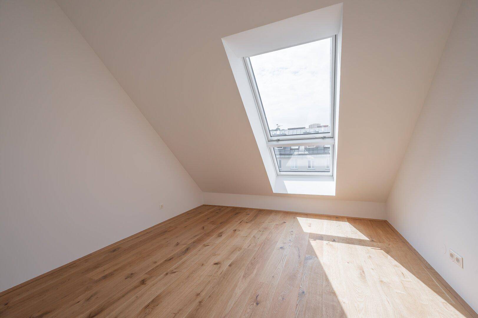Dachgeschossraum mit schrägem Dach und einem großen Dachfenster, das den Holzboden beleuchtet.