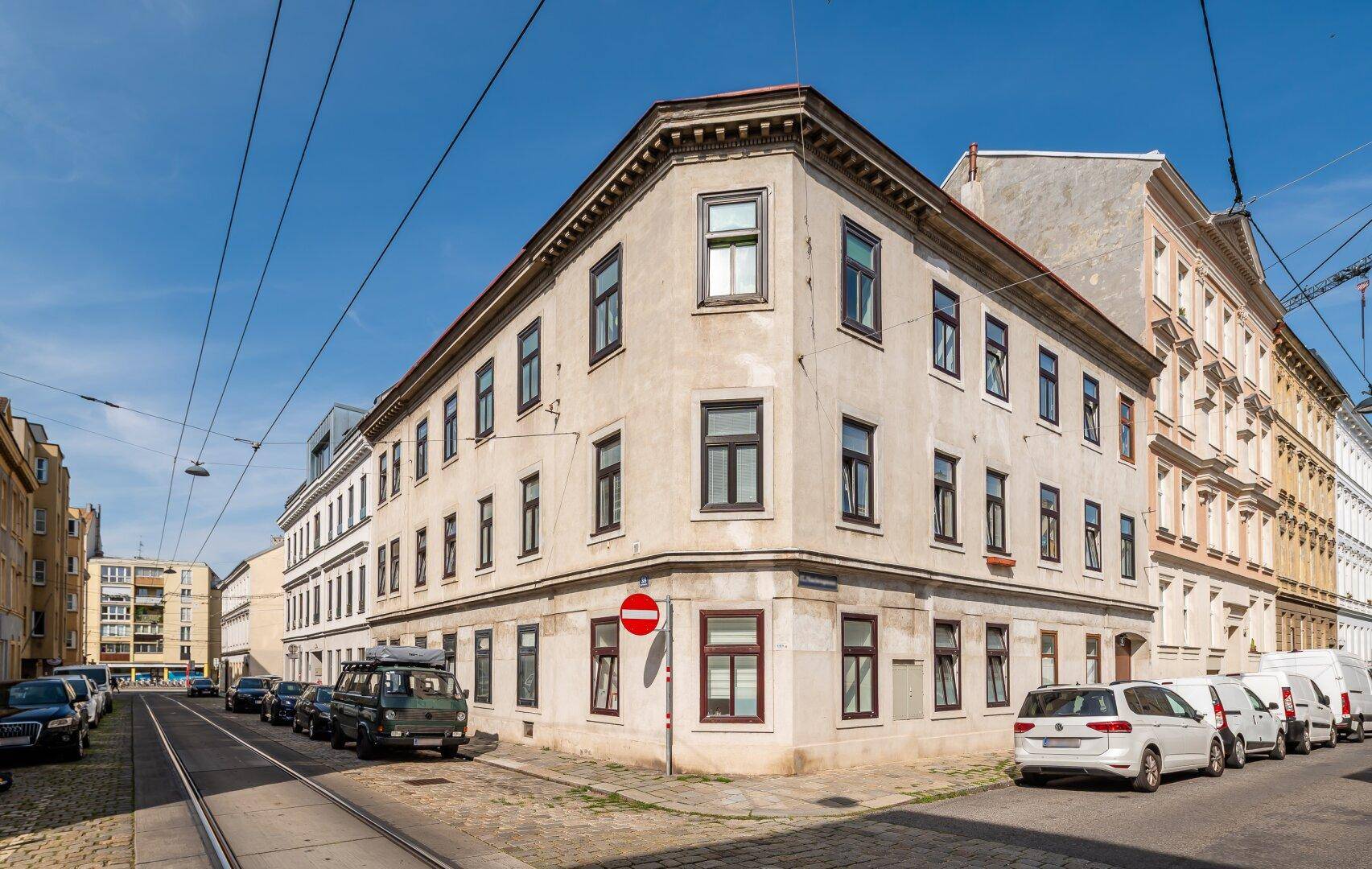 Eckgebäude in städtischer Umgebung mit geparkten Autos entlang der Straße unter blauem Himmel.