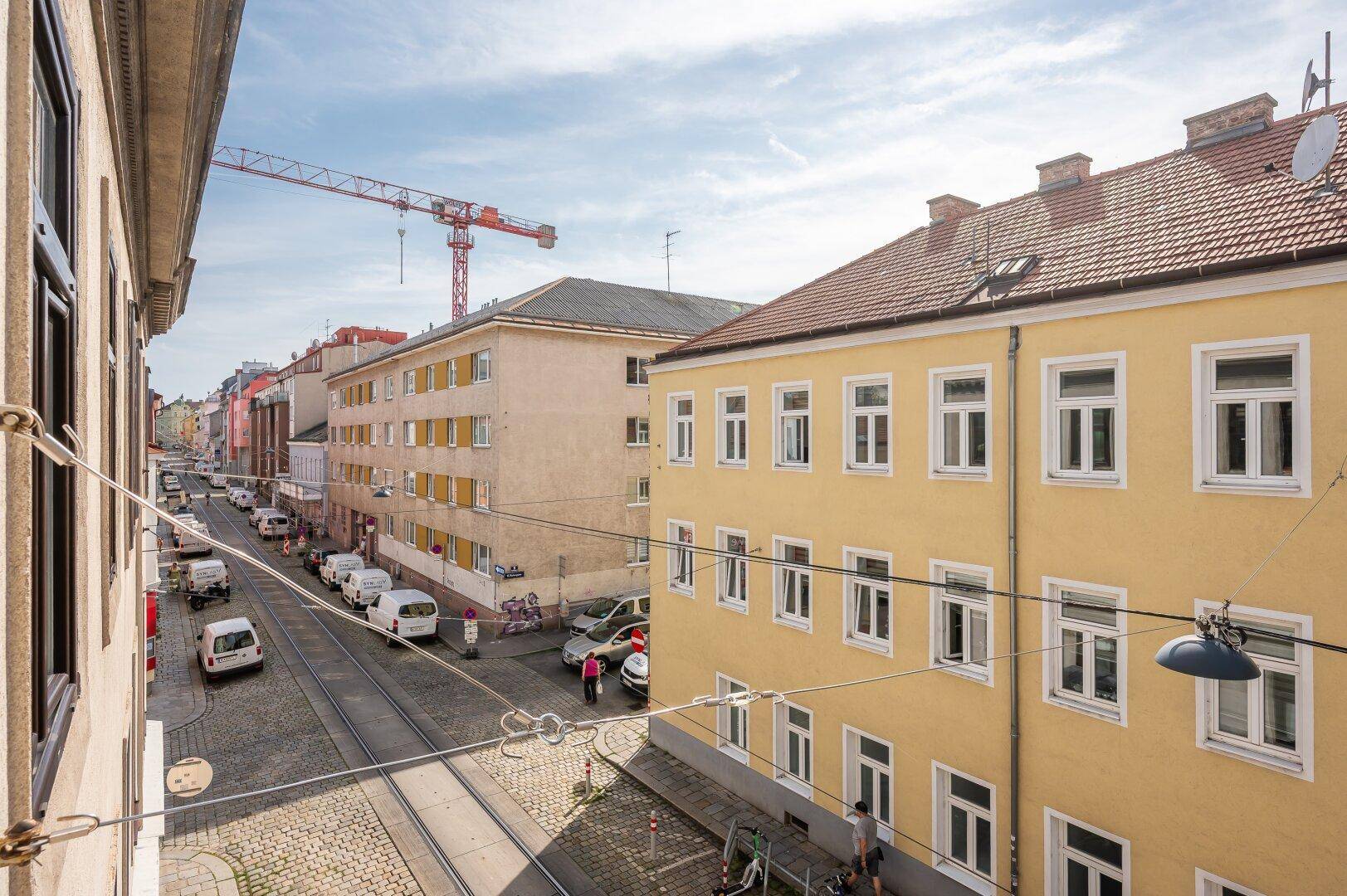 Blick von oben auf eine belebte Stadtstraße mit parkenden Autos und einem Baukran am Horizont.