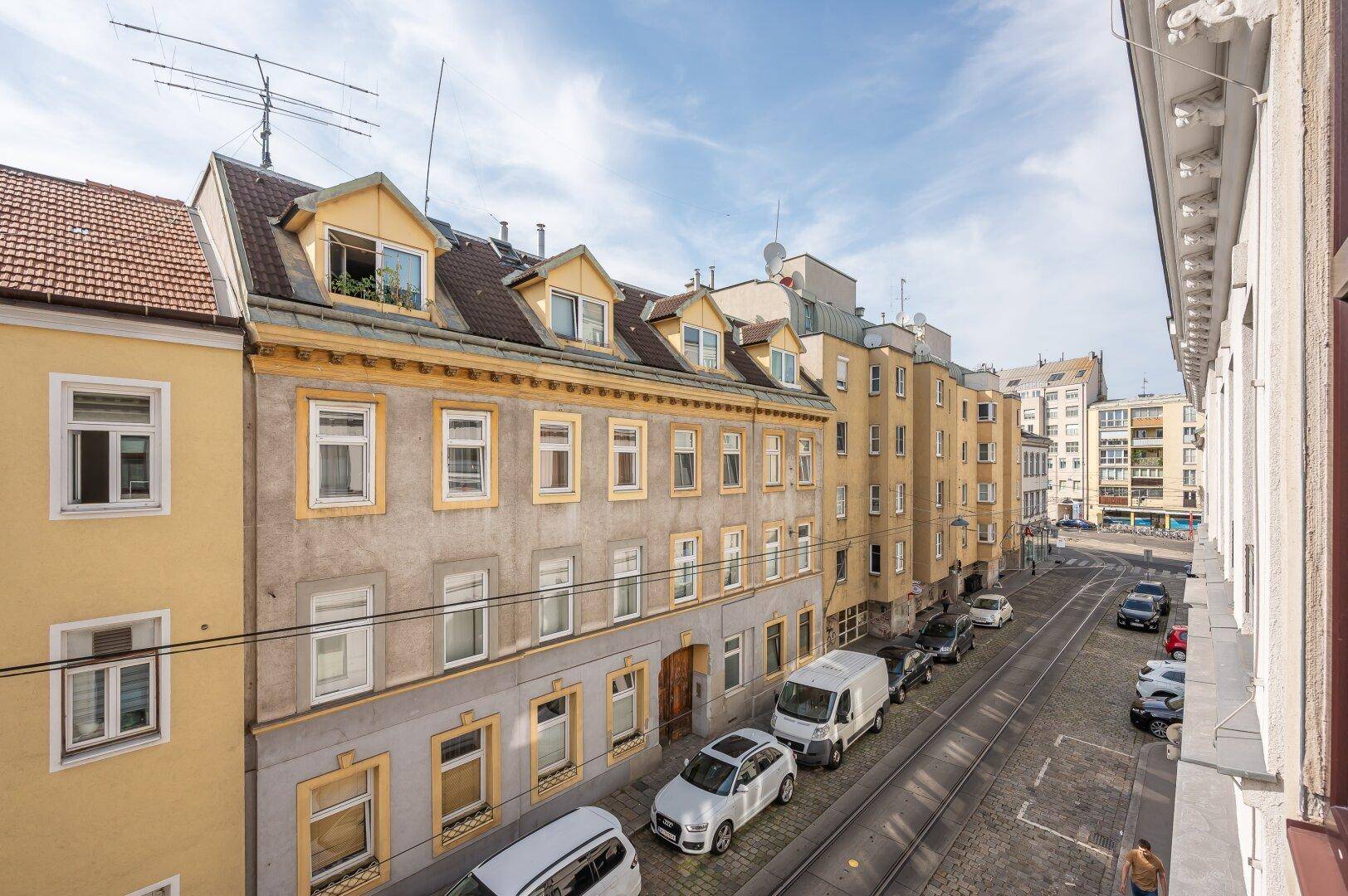Panoramablick auf eine städtische Straße mit historischen Gebäuden und parkenden Fahrzeugen.