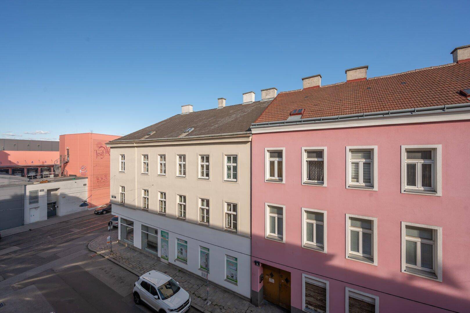 Straßenansicht mit historischen Gebäuden und parkenden Autos, die das städtische Umfeld zeigt.