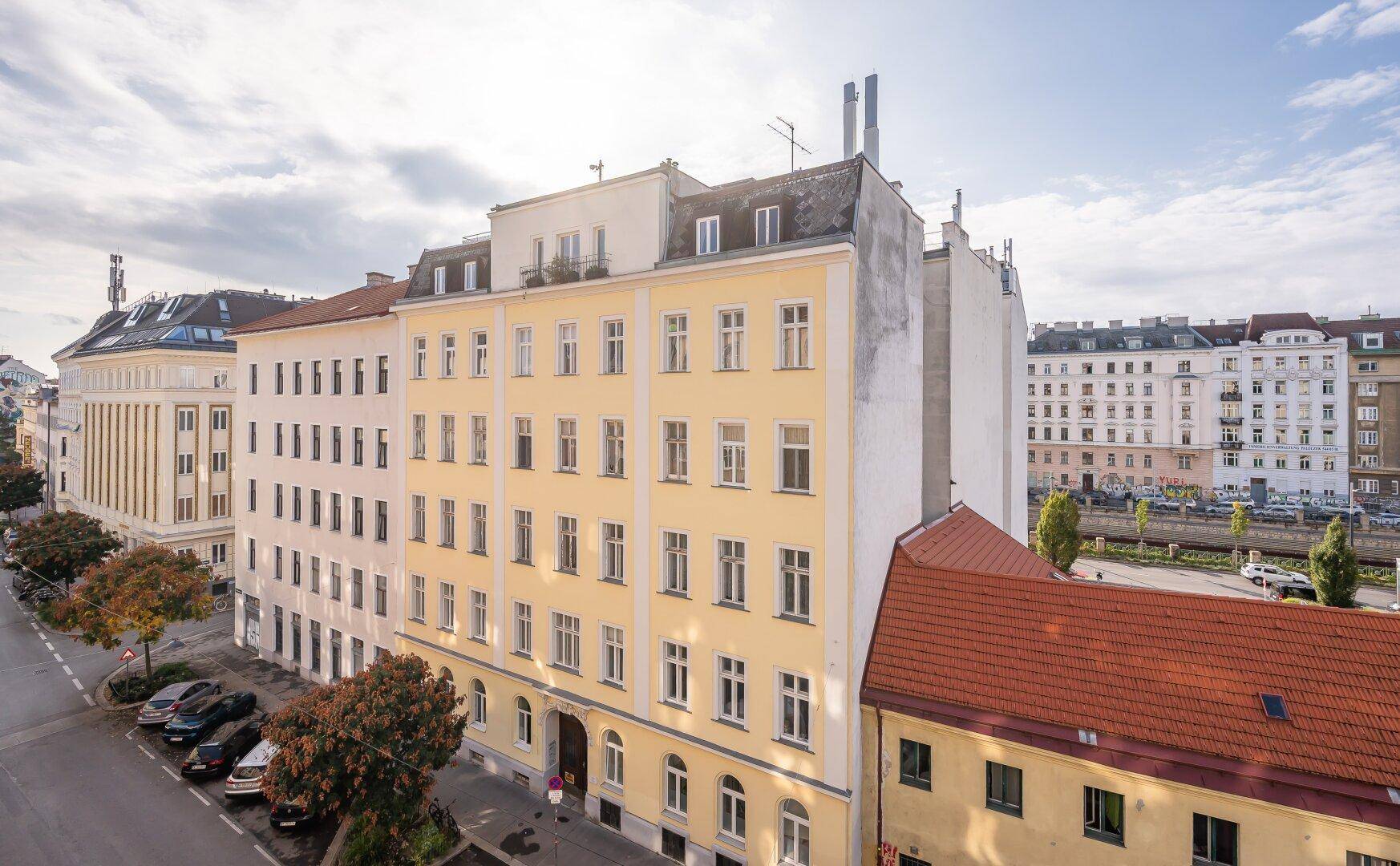 Historisches Gebäude mit gelber Fassade und vielen Fenstern in einer städtischen Umgebung.