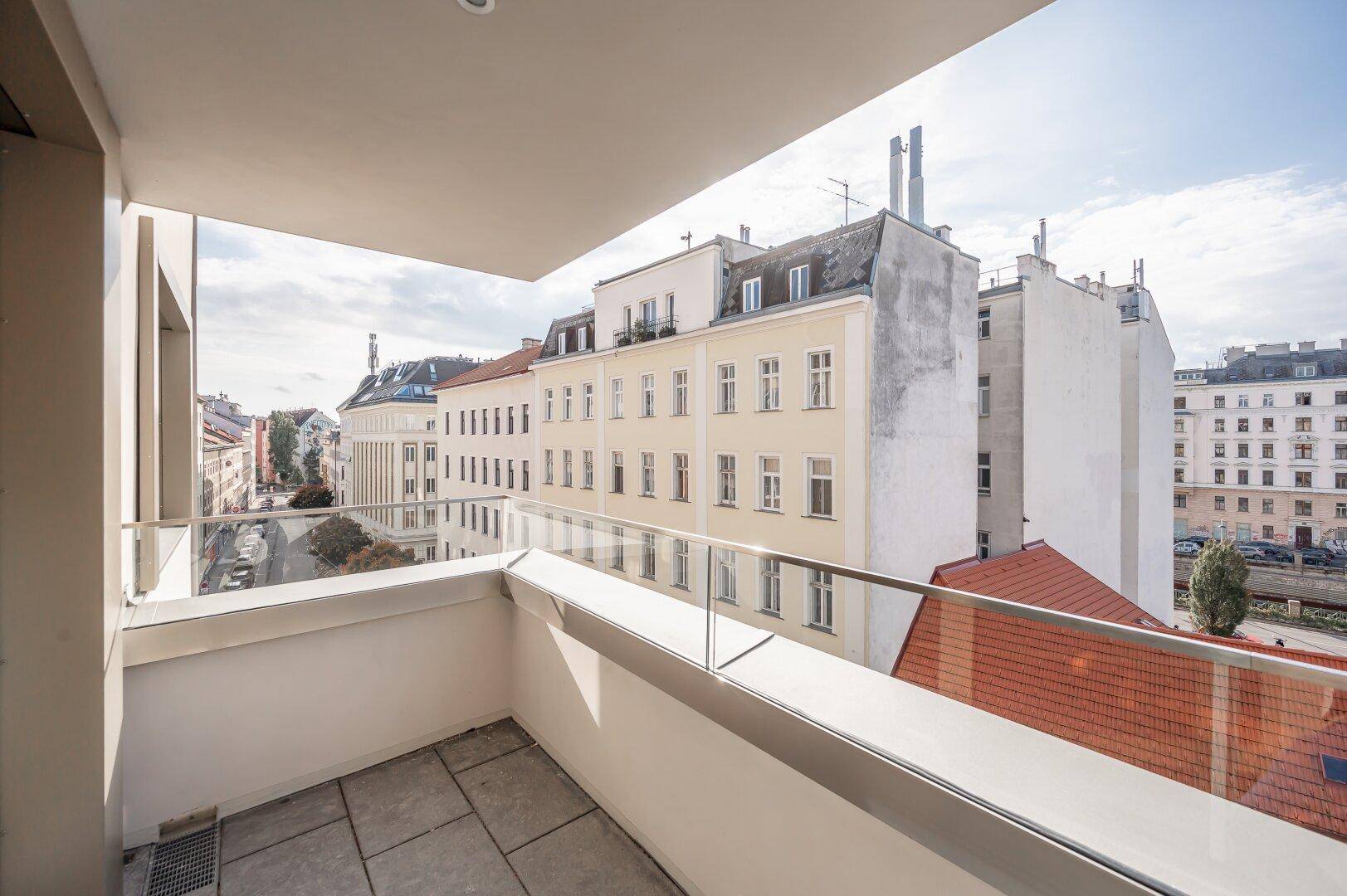 Heller Balkon mit Glasgeländer und weitem Blick über die Dächer der Stadt.