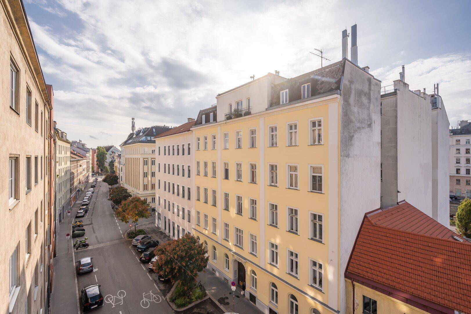 Panoramablick auf eine belebte Stadtstraße mit historischen Gebäuden und sonnigem Himmel.