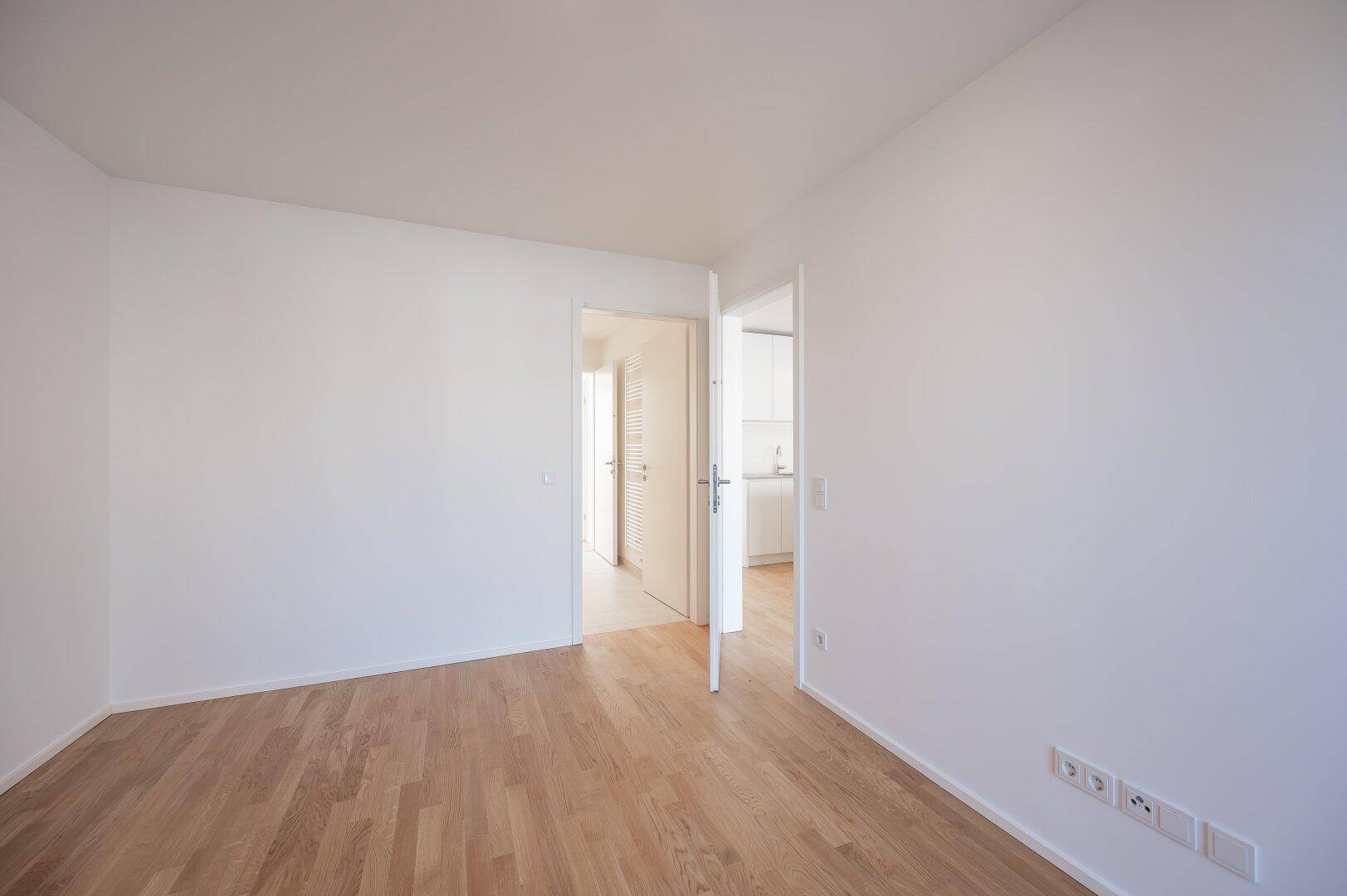 Heller, leerer Raum mit Holzboden und Türen, die zu anderen Bereichen der Wohnung führen.