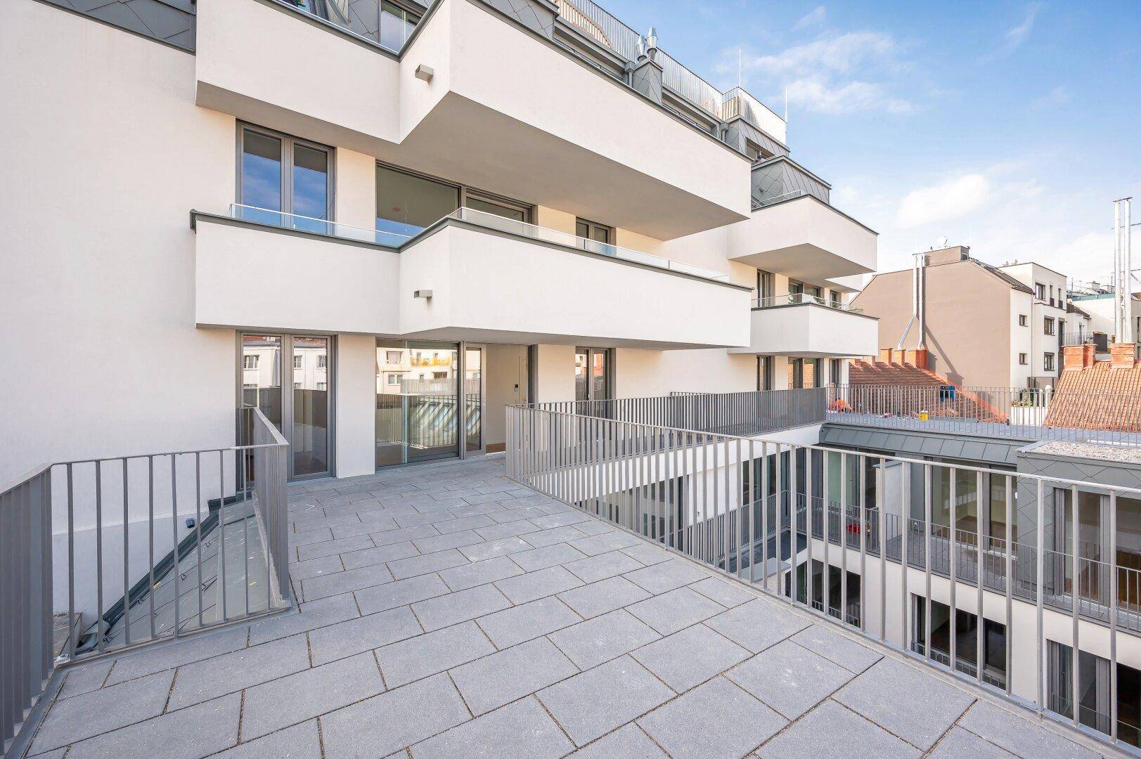 Weitläufige Terrasse mit Blick auf die moderne Architektur des Neubaus und die Umgebung.
