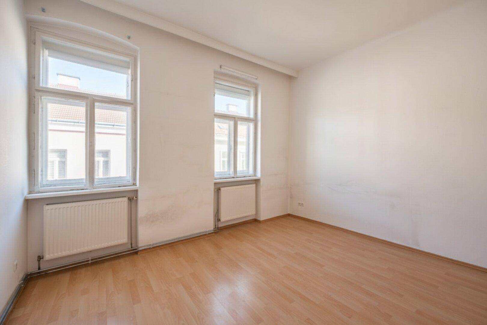 Unmöbliertes Zimmer mit Holzboden, weißen Wänden und zwei Fenstern, bereit zur individuellen Gestaltung.
