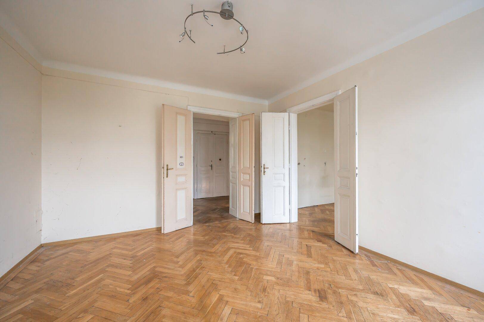 Geräumiges Zimmer mit Fischgrätparkett und mehreren Türen, bereit zur Renovierung.