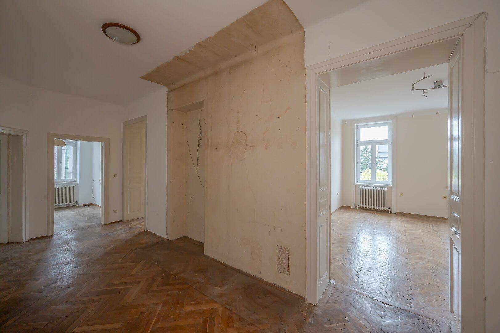 Flur mit Fischgrätparkett und sichtbaren Renovierungsspuren, der zu weiteren Räumen führt.