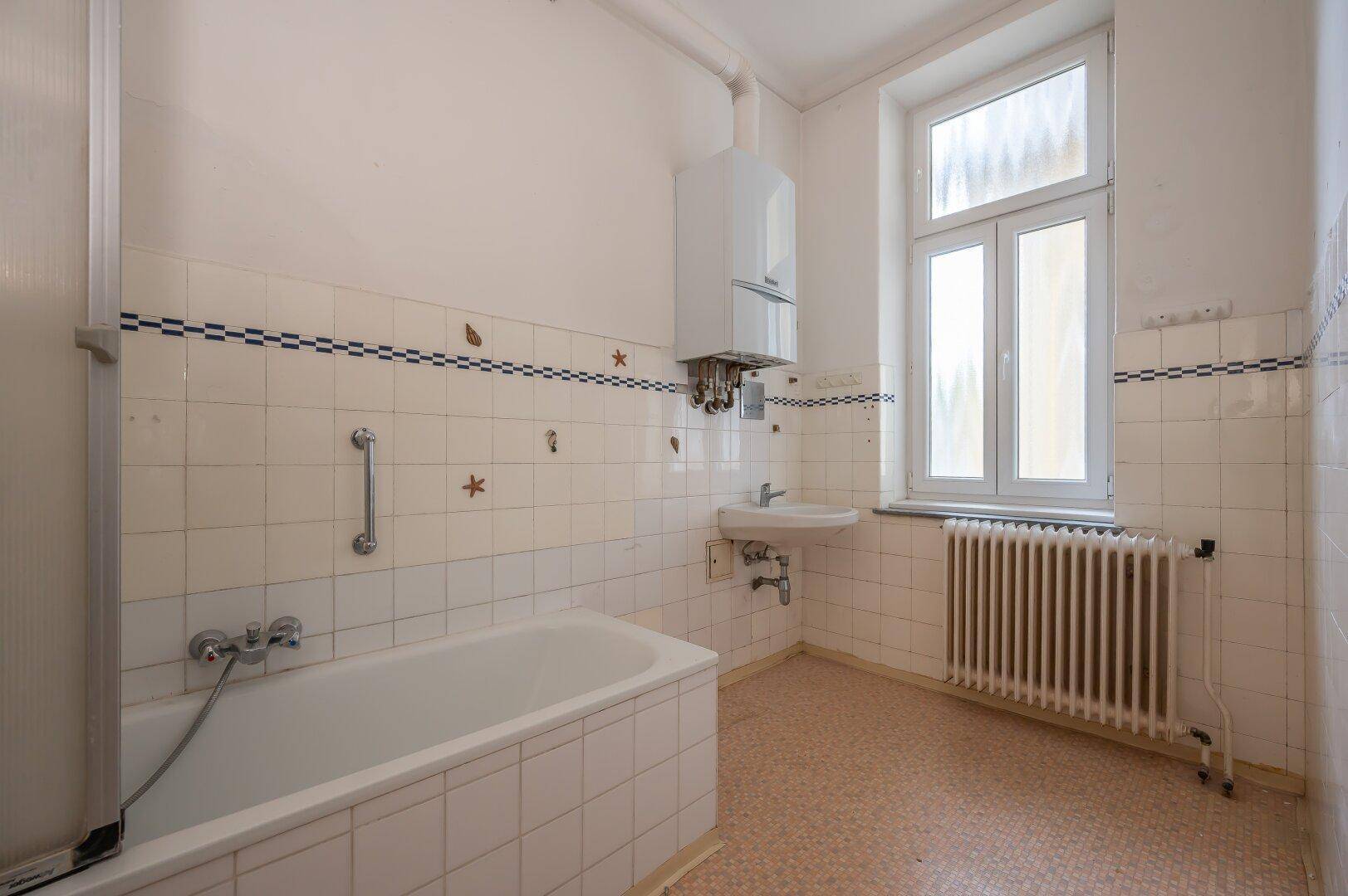 Helles Badezimmer mit Badewanne, Fenster und Wandfliesen im Vintage-Stil.