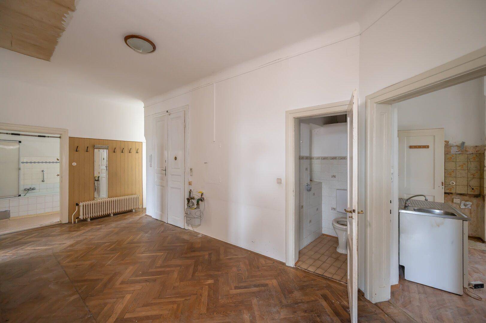 Flur mit Fischgrätparkett und Zugang zu Bad und WC, mit Renovierungsbedarf.