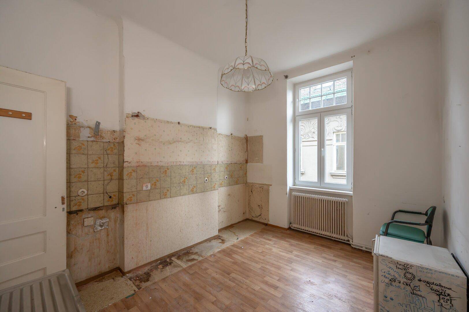 Leere Küche mit alten Fliesen und Fenster, bereit für eine komplette Neugestaltung.