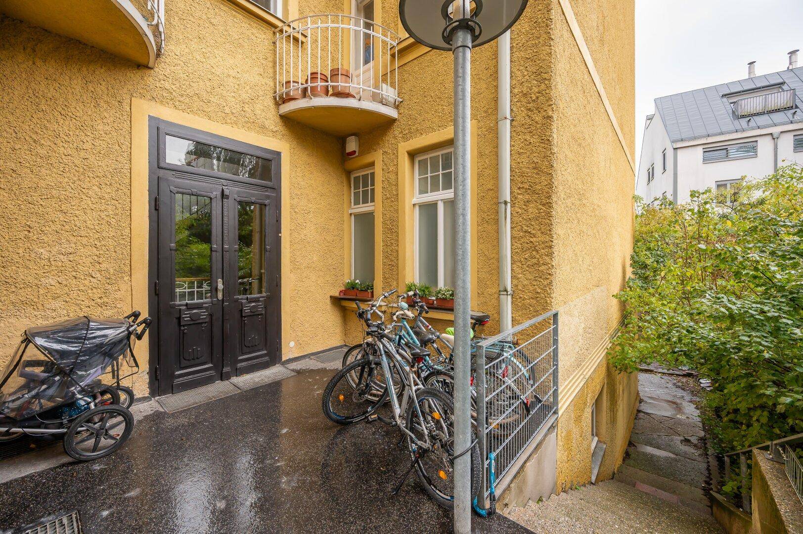 Eingangsbereich des Gebäudes mit Fahrrädern, Kinderwagen und Treppenzugang.