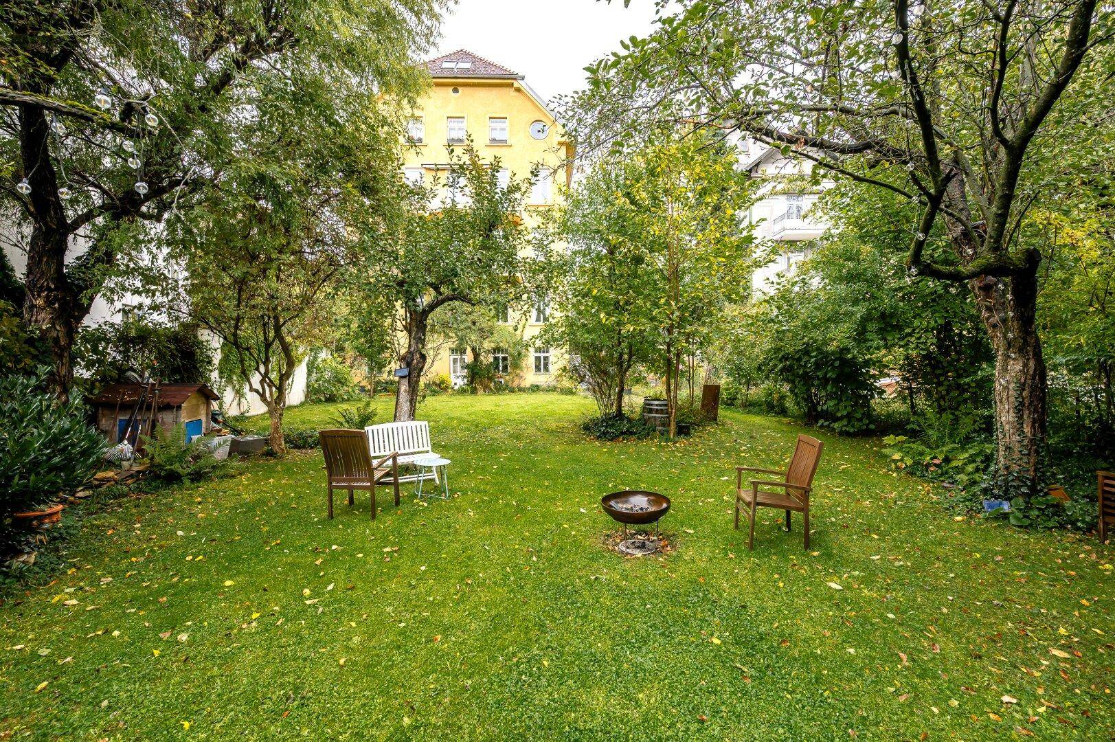 Gepflegter Garten mit Rasenfläche, Bäumen und Sitzgelegenheiten, umgeben von Natur.
