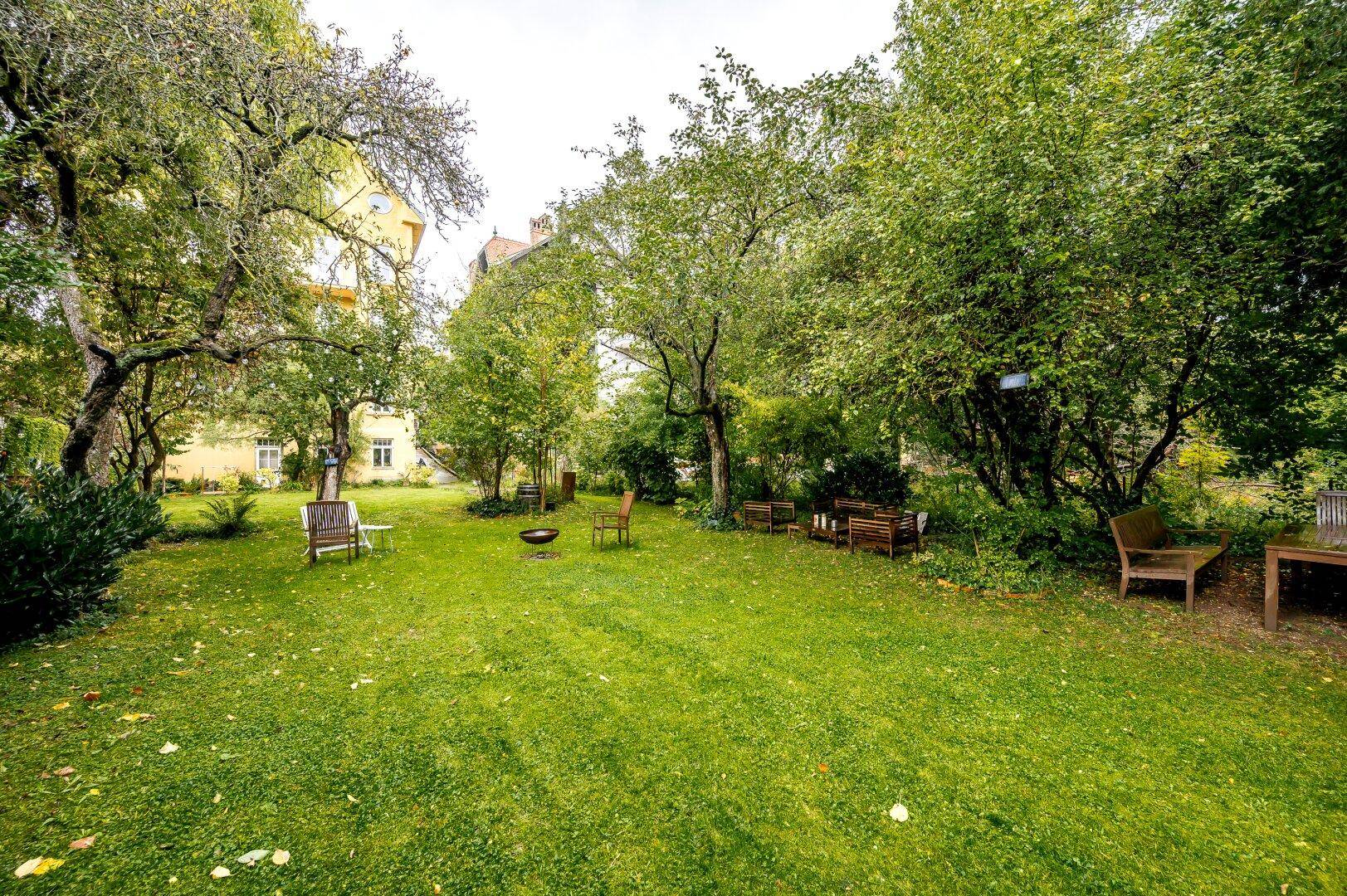 Weitläufiger Garten mit Rasen, Bäumen und einem Feuerkorb, ideal zum Entspannen.