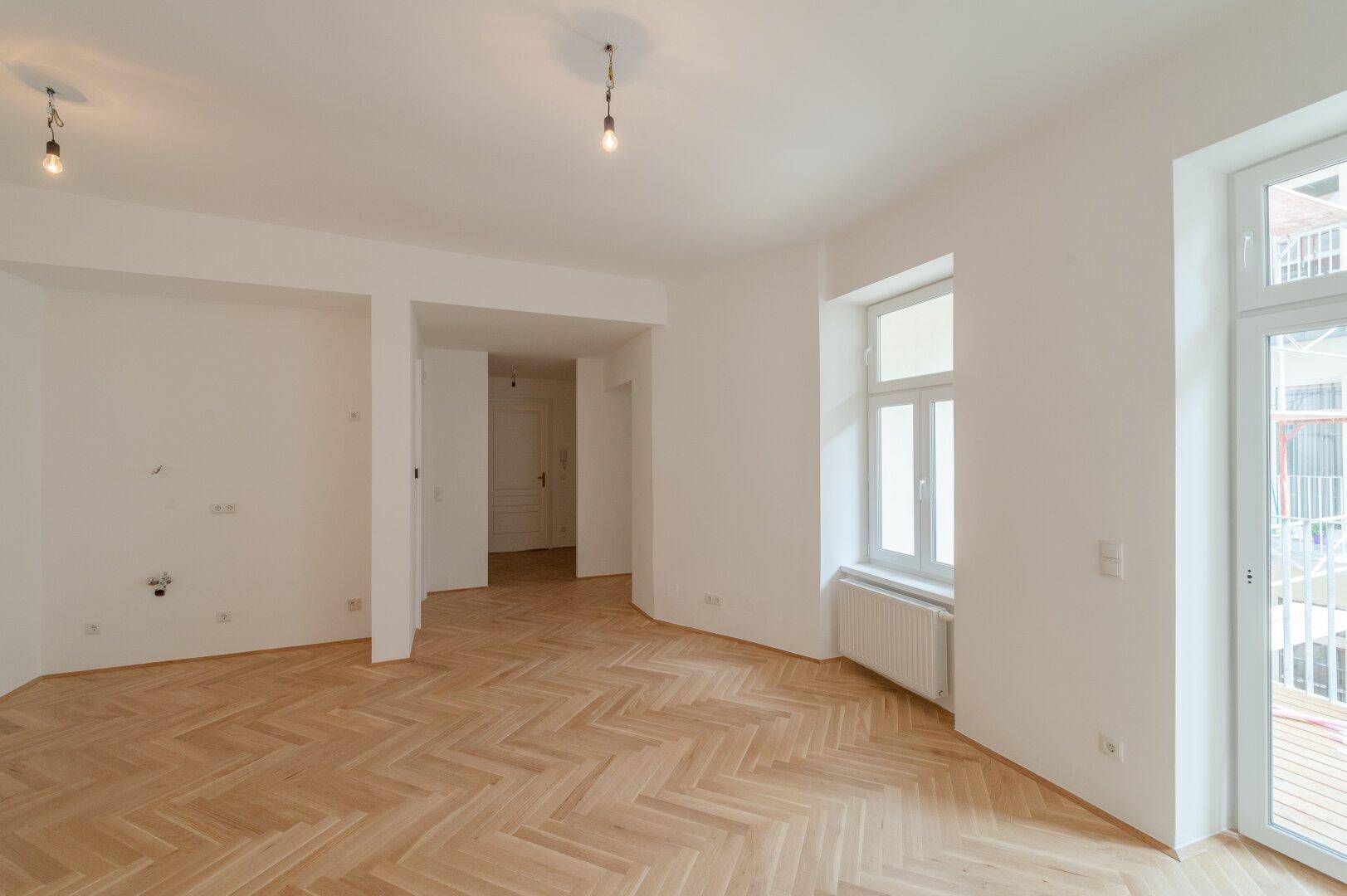 Heller Wohnraum mit elegantem Fischgrätparkett und Zugang zu einem Balkon.