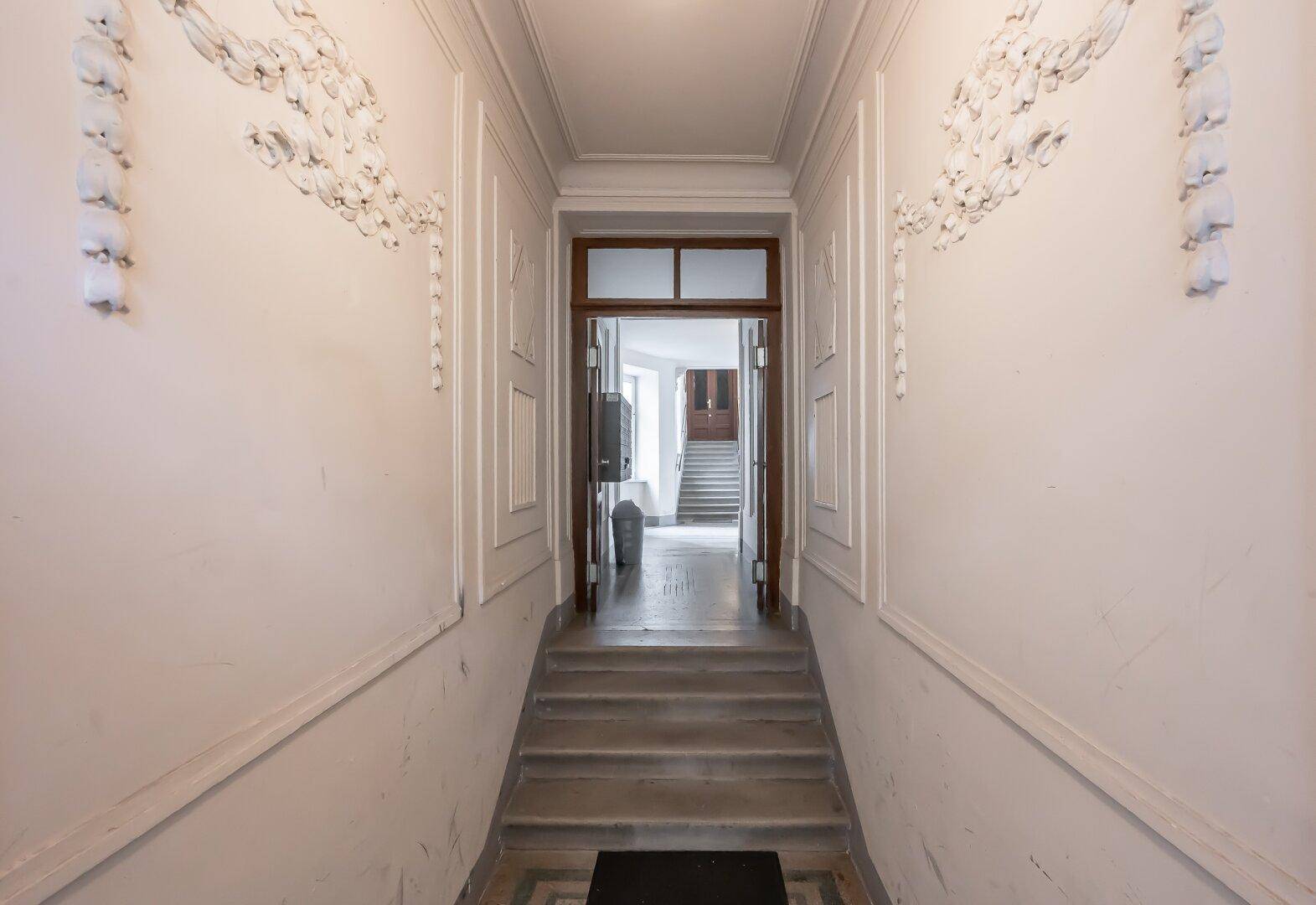 Historischer Eingangsbereich mit Stuckverzierungen, hohen Decken und Zugang zum Treppenhaus.