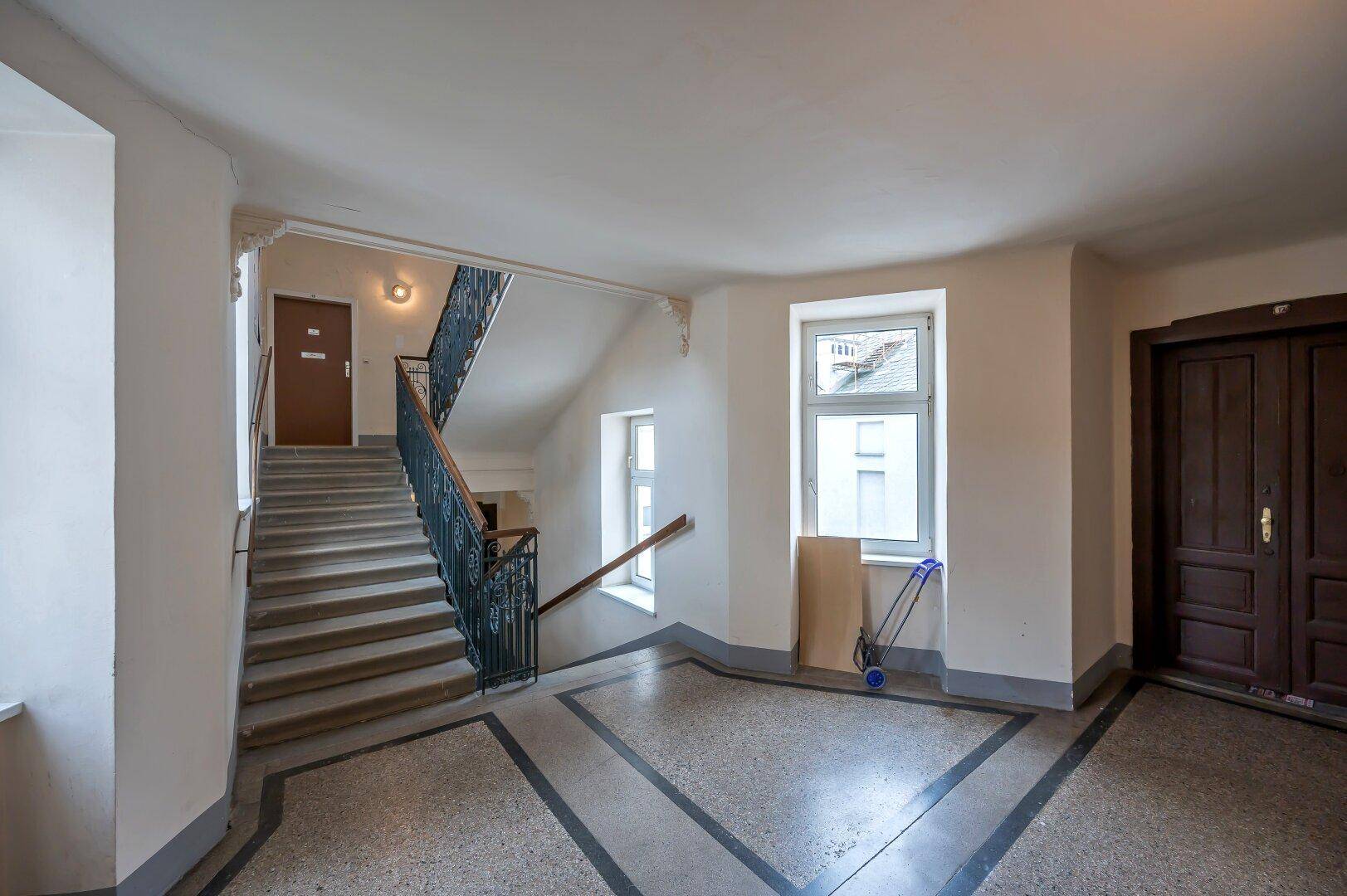 Geräumiges Treppenhaus mit Terrazzoboden, schmiedeeisernem Geländer und großen Fenstern.