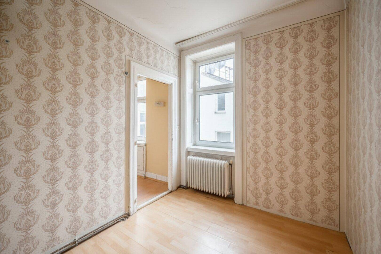 Kleineres Zimmer mit Laminatboden, gemusterter Tapete und Fenster mit Blick nach draußen.