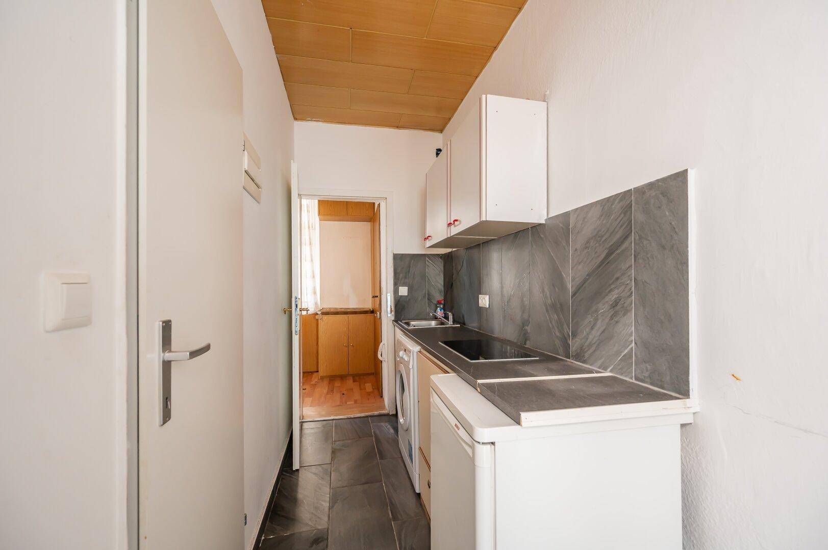Schmale Küche mit Waschmaschine, Kühlschrank und dunklen Fliesen.