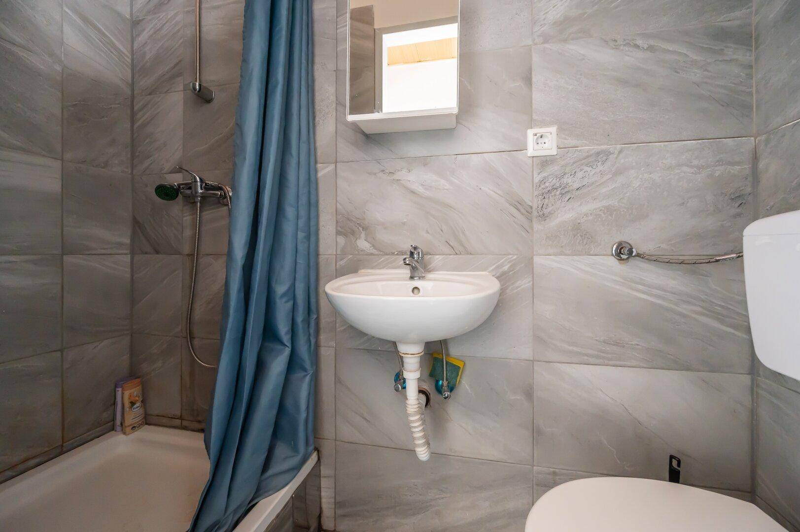 Kleines Badezimmer mit Badewanne, Dusche und grauen Wandfliesen.