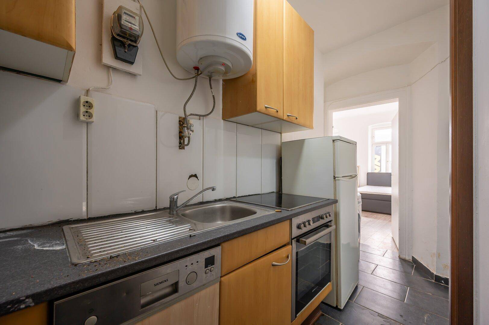 Funktionale, aber renovierungsbedürftige Küche mit Spüle, Herd, Geschirrspüler und Kühlschrank.