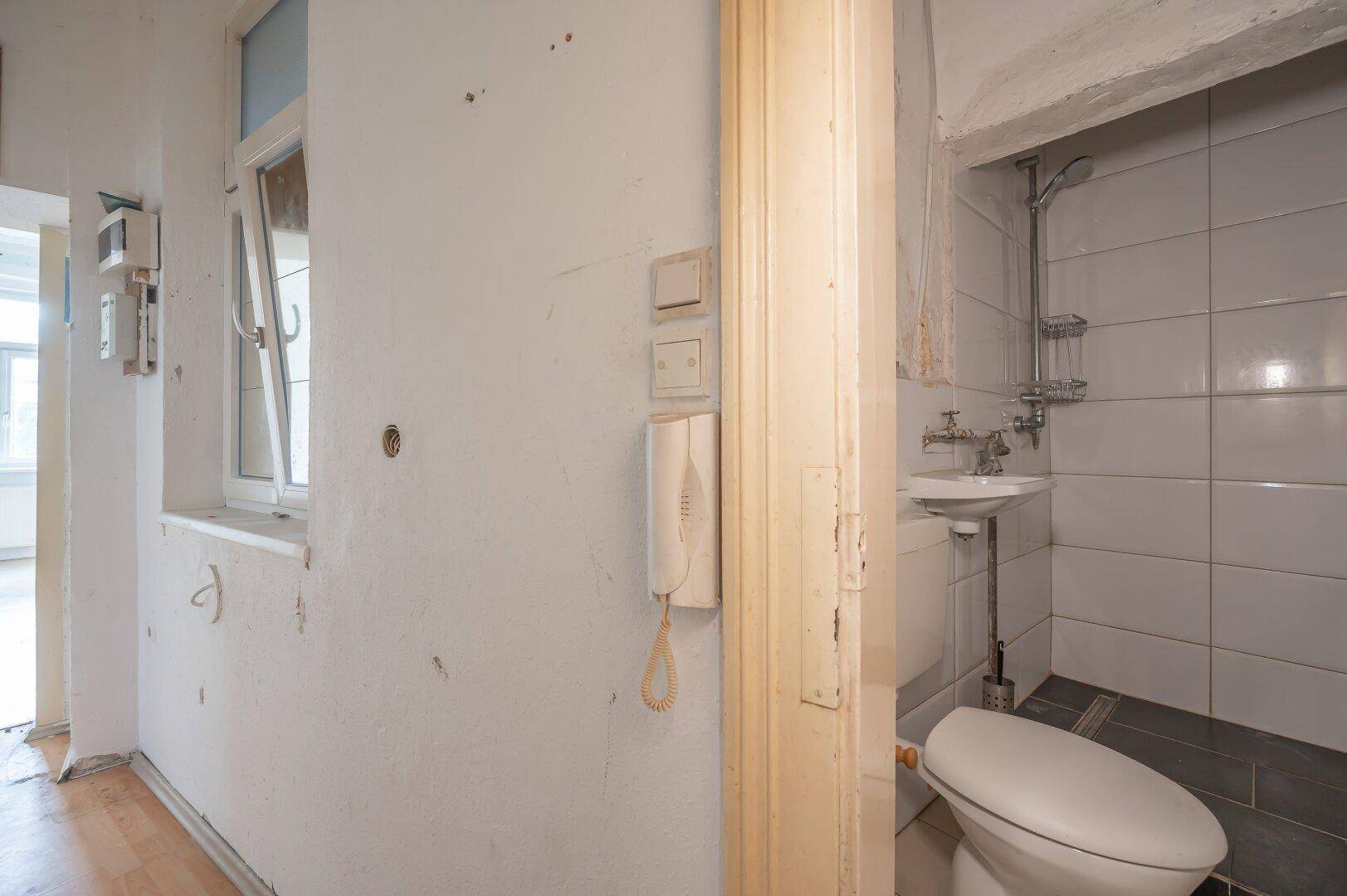 Kleines Badezimmer mit WC, Waschbecken und Duschvorrichtung, das dringend renoviert werden muss.