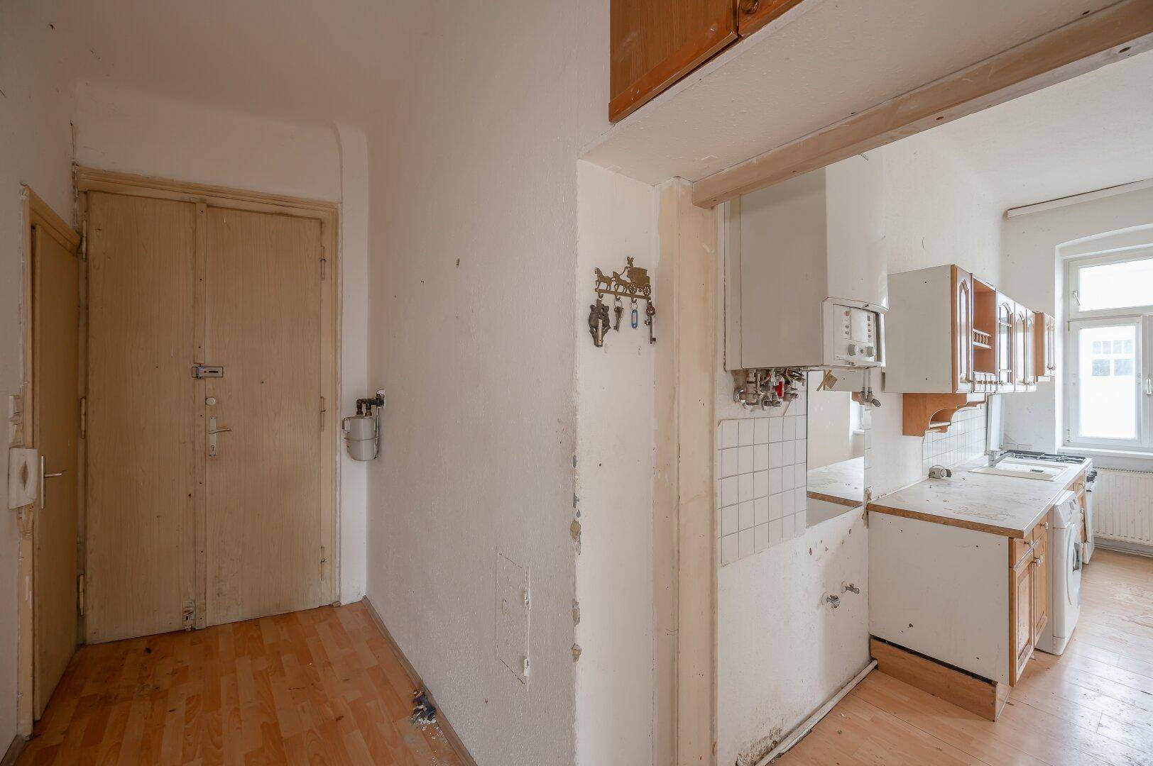 Eingangsbereich mit Laminatboden und Blick in die Küche, der den Renovierungsbedarf der Immobilie zeigt.