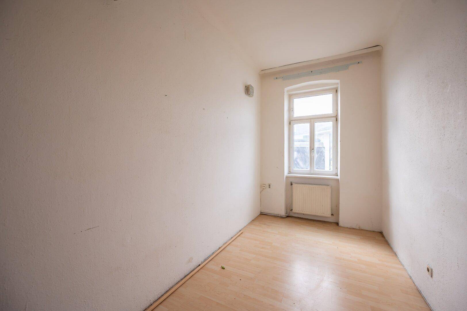 Kleiner, heller Raum mit einem Fenster und Laminatboden, geeignet als Schlaf- oder Arbeitszimmer.