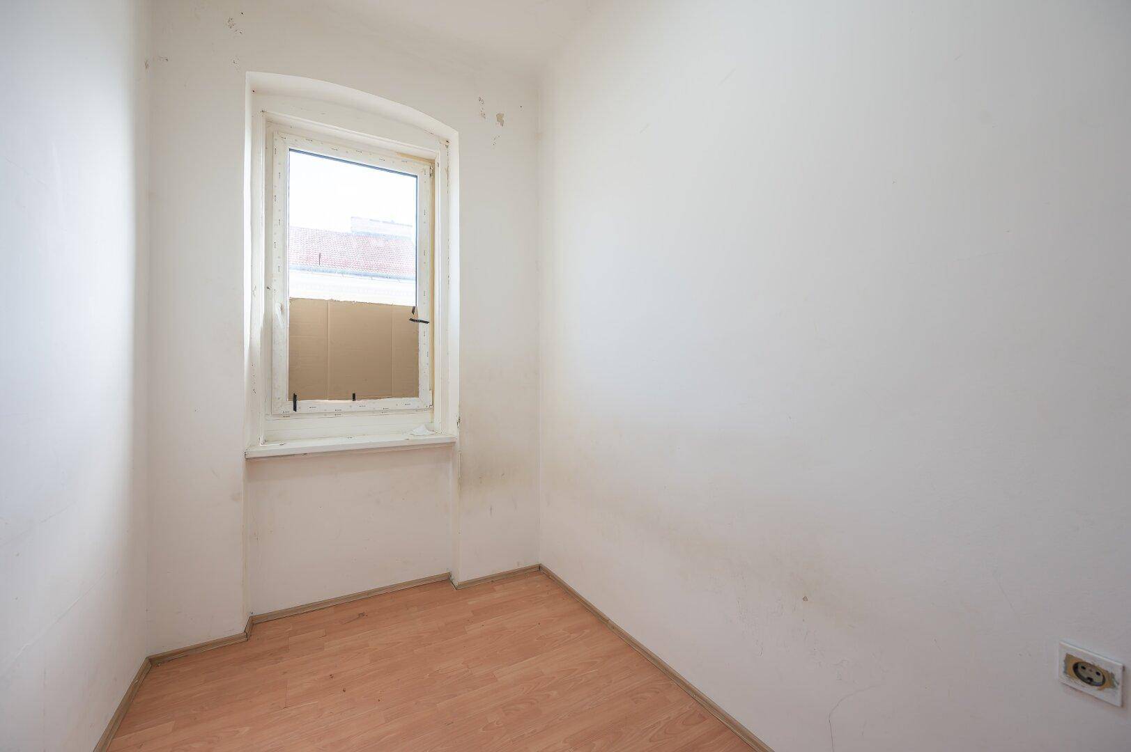 Helles Zimmer mit Laminatboden und einem Fenster, das auf eine Renovierung wartet.