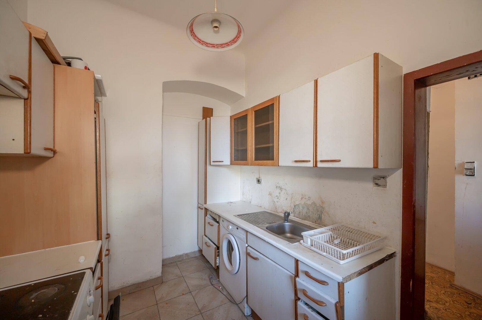 Veraltete Küche mit einfachen Schränken, Spüle und Waschmaschine, die eine Modernisierung benötigt.