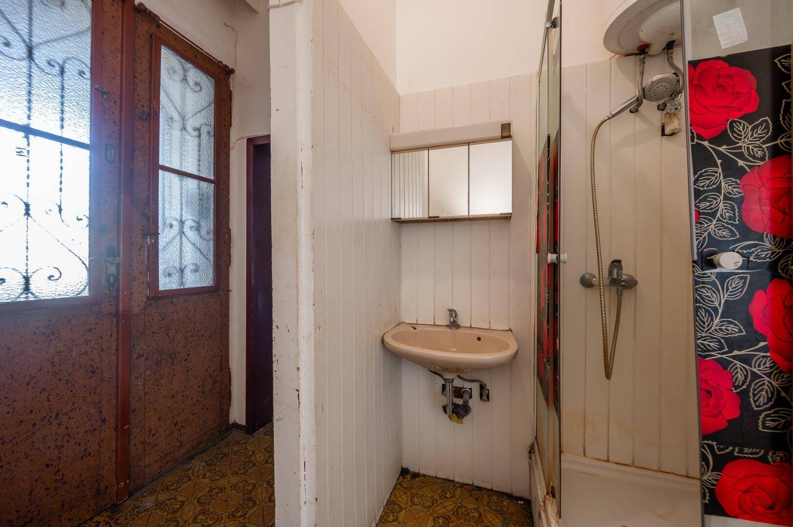 Einfaches Badezimmer mit Waschbecken, Spiegelschrank und Duschkabine, das eine Modernisierung erfordert.
