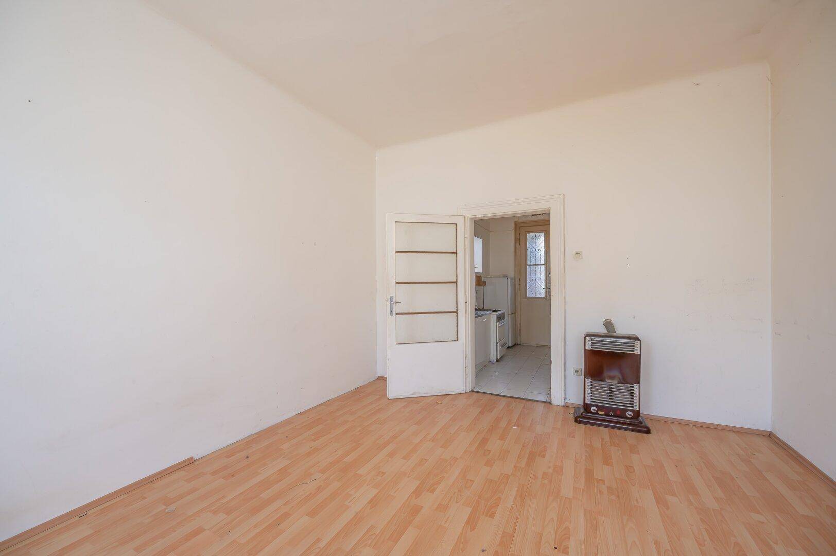 Leeres Zimmer mit Laminatboden, einem Ofen und Zugang zu einem weiteren Raum.