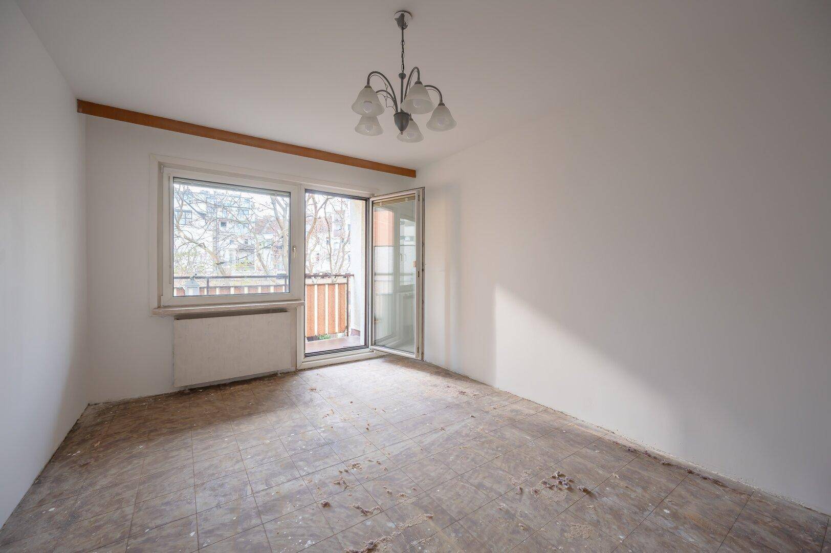 Leeres Zimmer mit Zugang zum Balkon und einfacher Deckenleuchte, bereit für Renovierung.