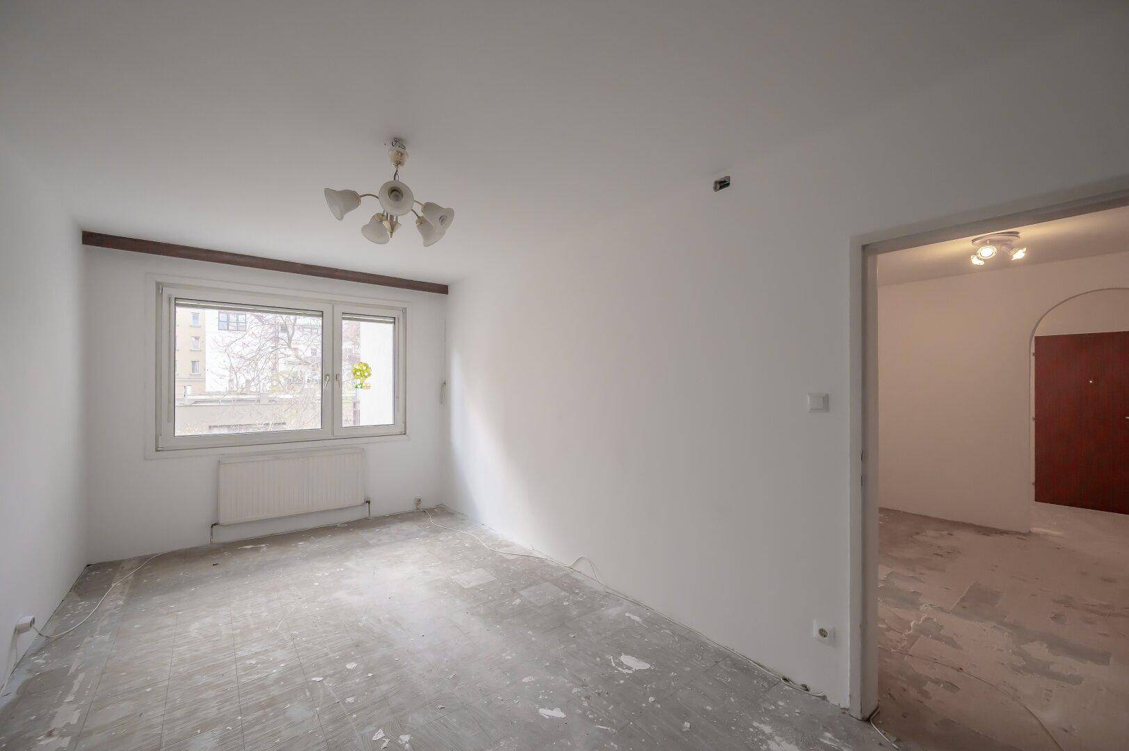 Leeres Zimmer mit Fenster und einfacher Deckenleuchte, bereit für neue Bodenbeläge.