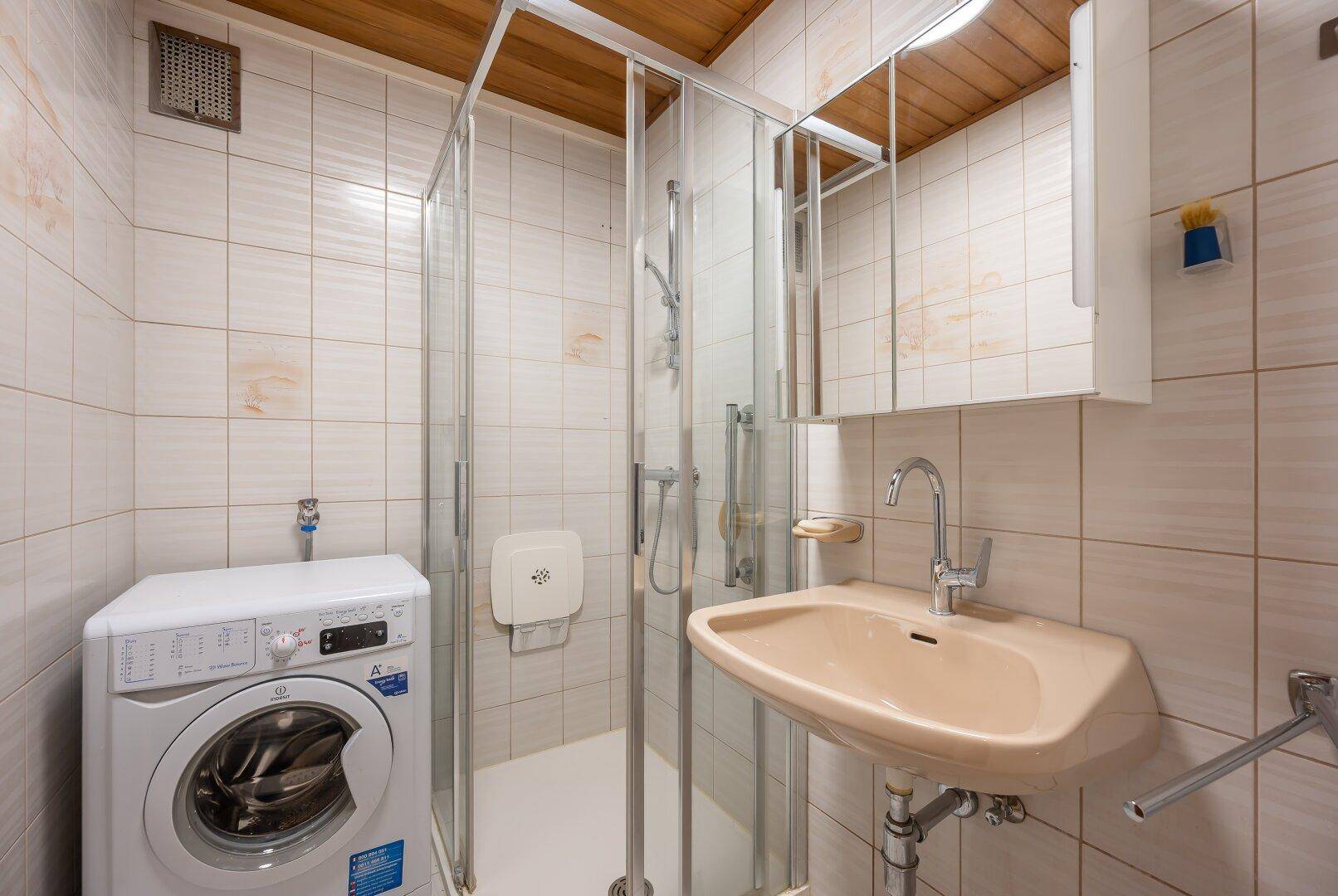 Kleines Badezimmer mit Duschkabine, Waschbecken und Waschmaschine, mit Holzdecke.