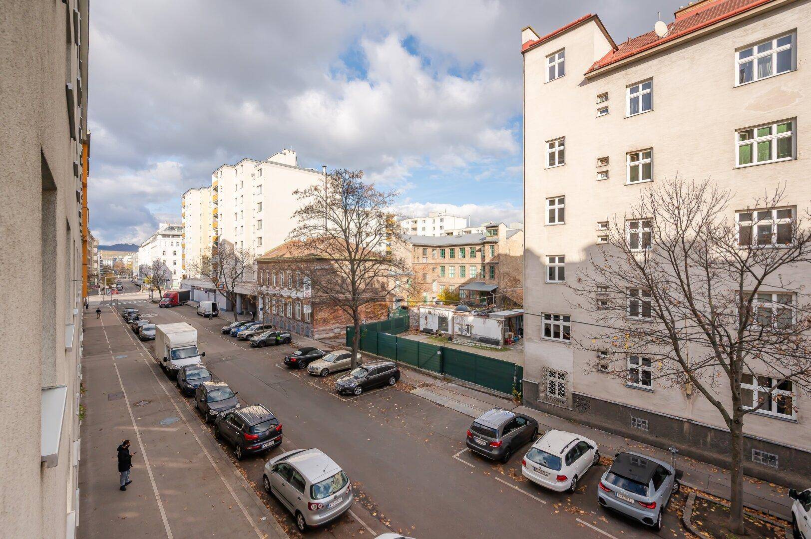 Blick auf eine Wohnstraße mit parkenden Autos und traditionellen Gebäuden unter bewölktem Himmel.