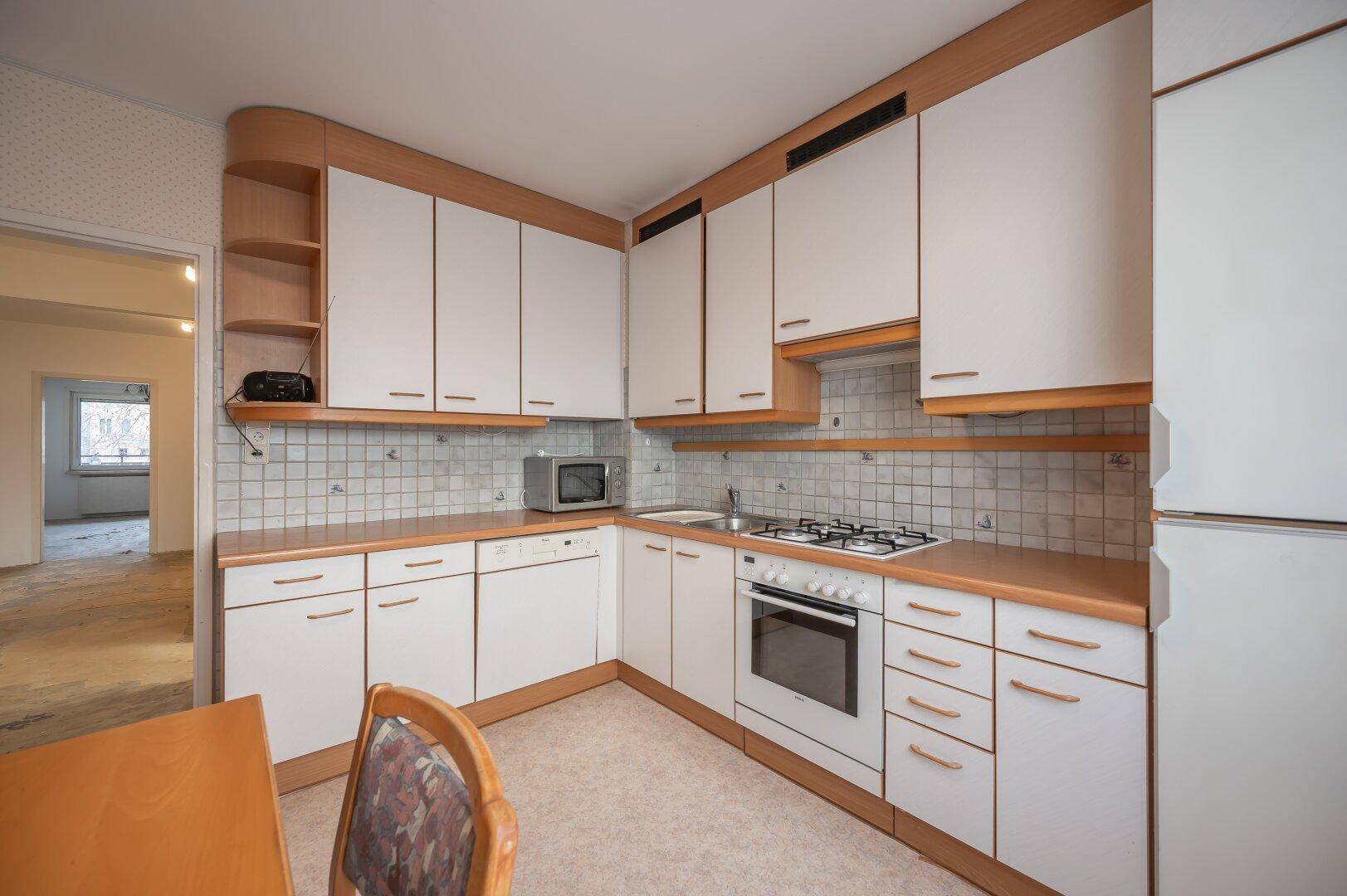 Winkelküche mit weißen Schränken und Holzdetails, ausgestattet mit Mikrowelle und Spülbecken.