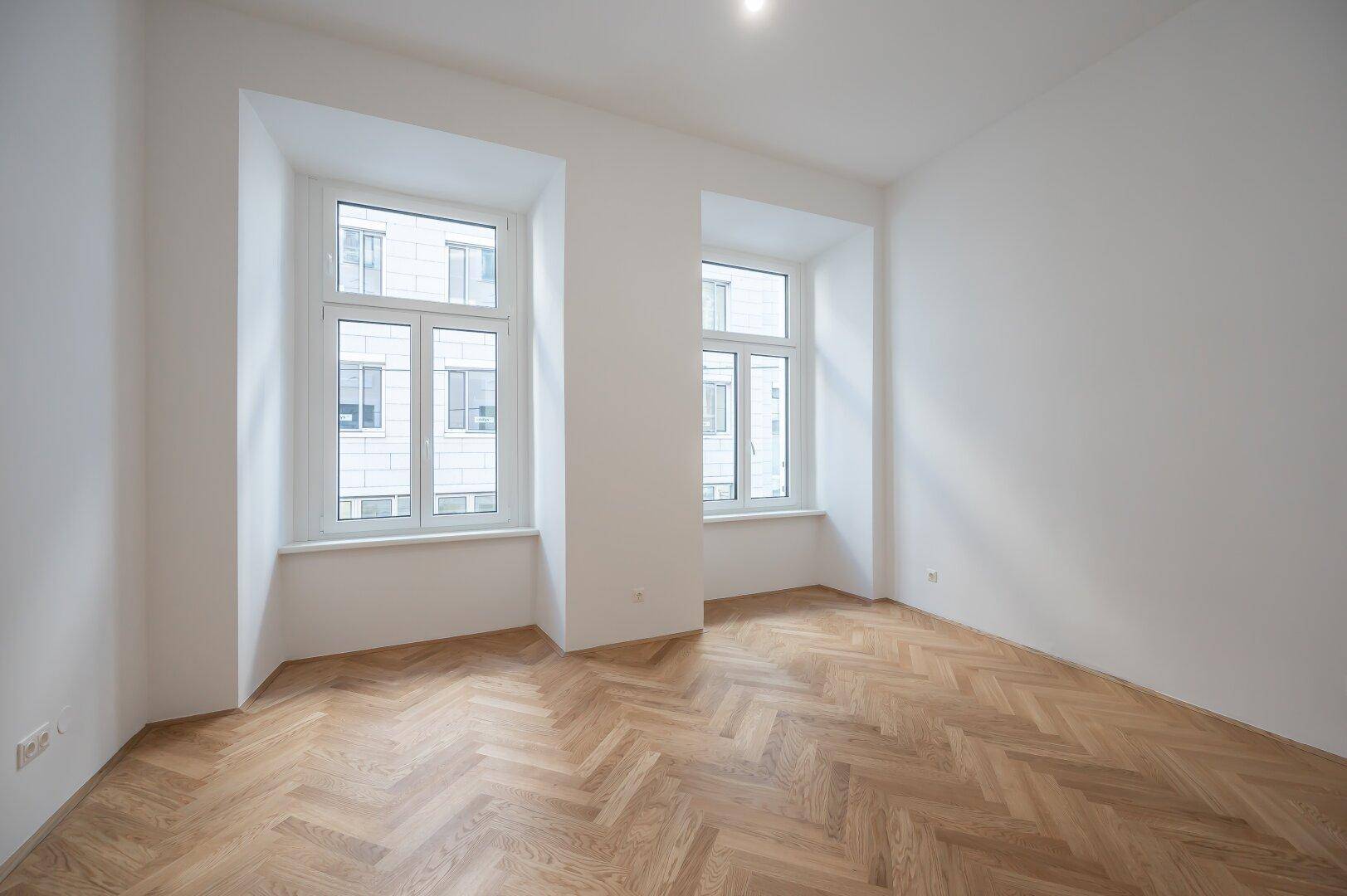 Lichtdurchfluteter Raum mit großen Fenstern und Fischgrätparkett, ideal für Wohn- oder Schlafzimmer.