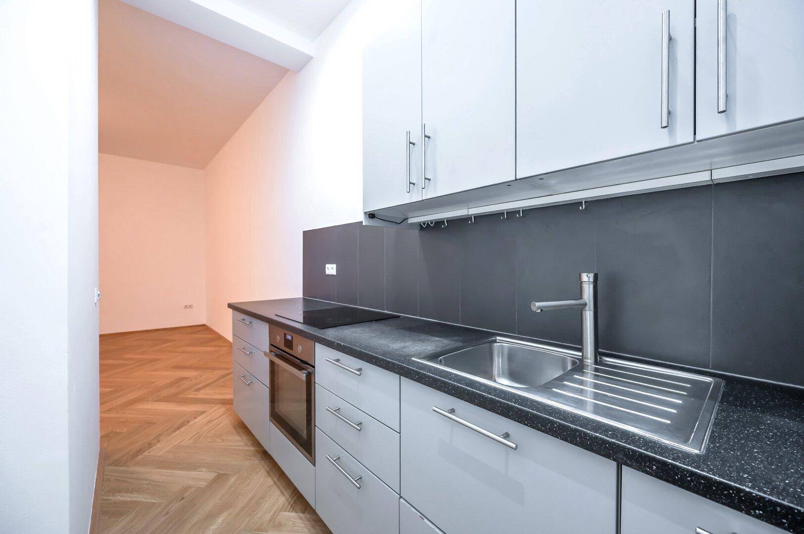 Moderne Einbauküche mit hellgrauen Schränken, dunkler Arbeitsplatte und integrierten Geräten.
