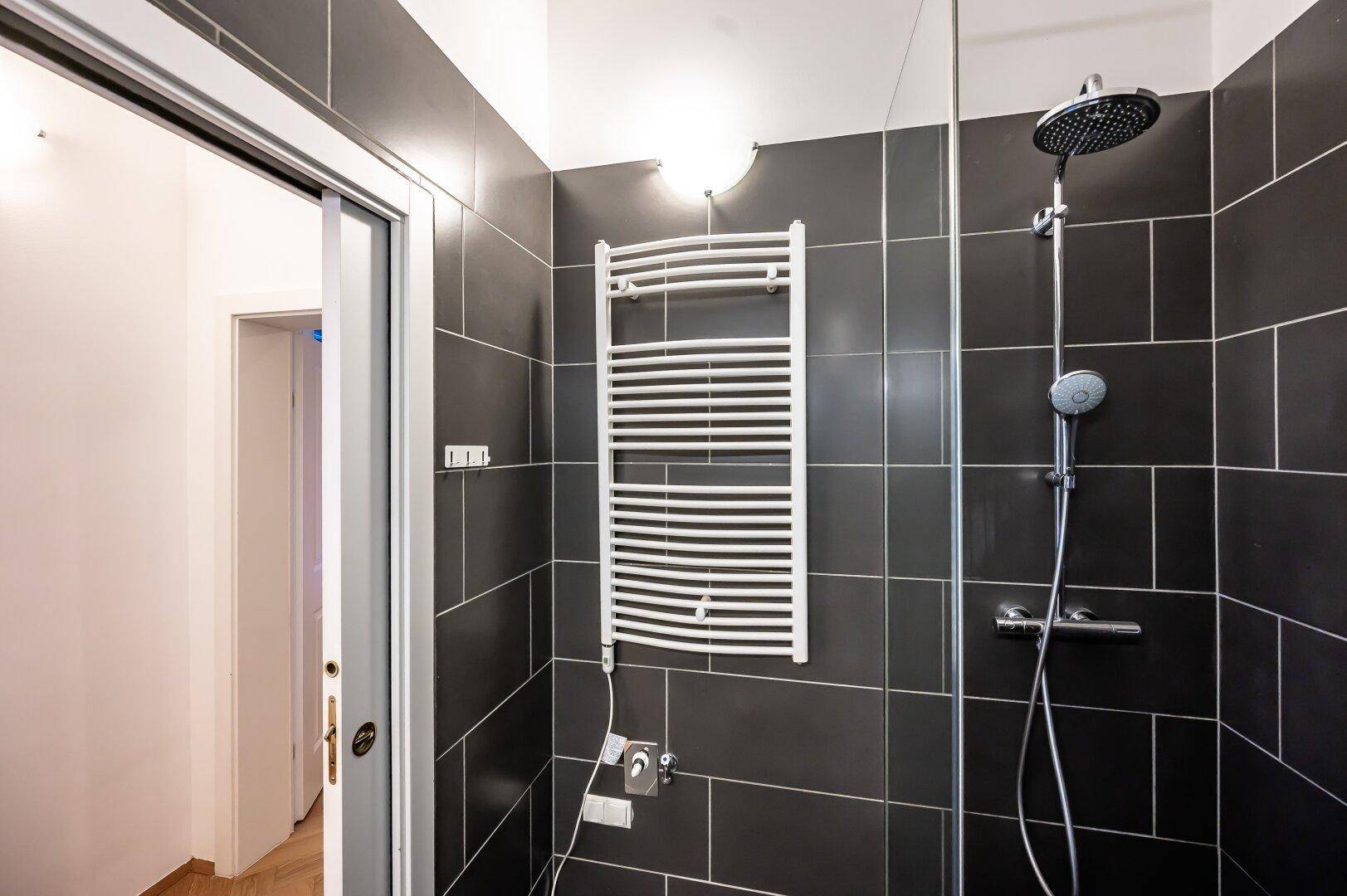 Duschbereich im modernen Badezimmer mit dunklen Fliesen und praktischem Handtuchheizkörper.
