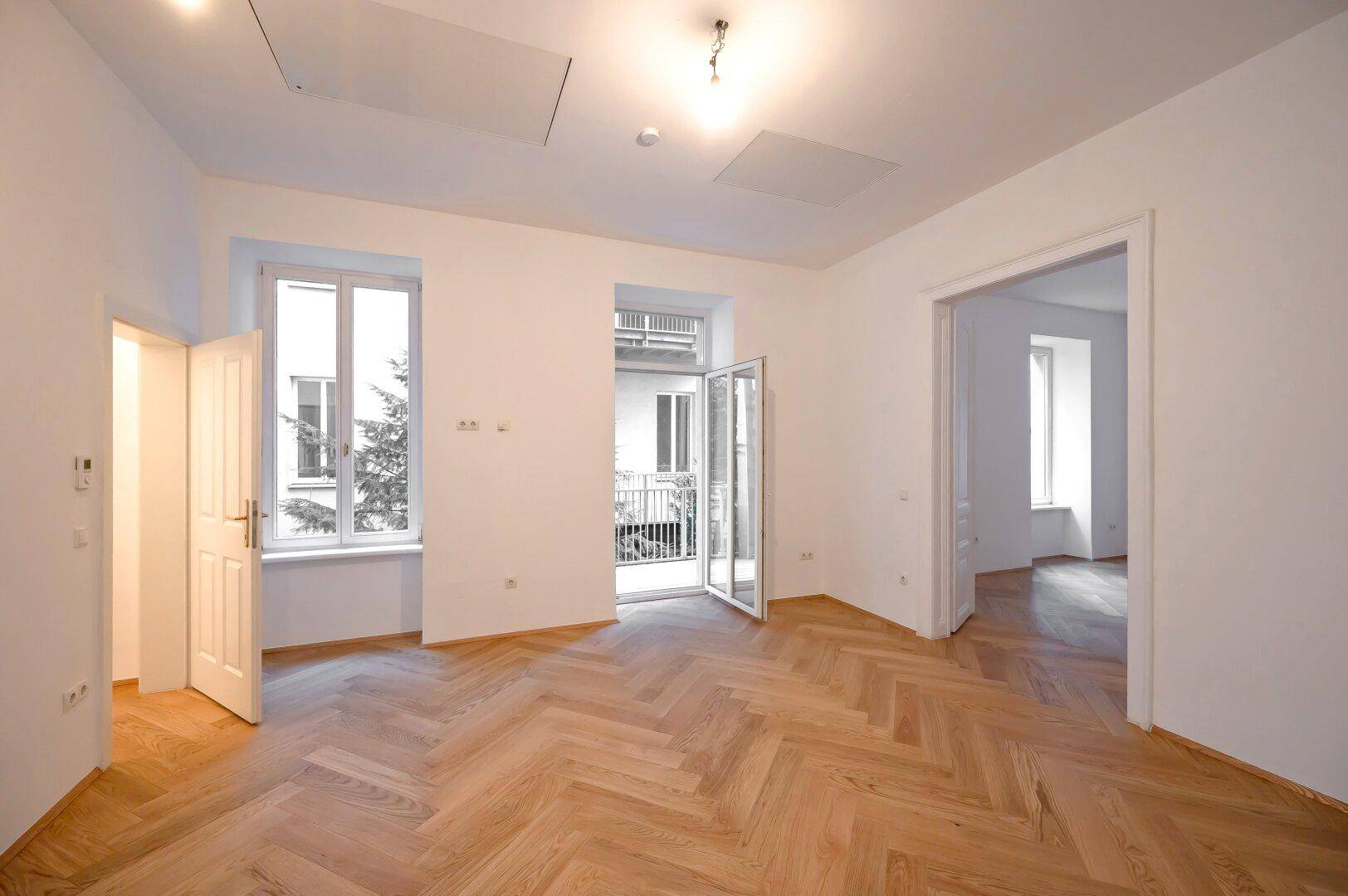 Heller Wohnraum mit Fischgrätparkett und Zugang zu einem Balkon, der viel Licht bietet.