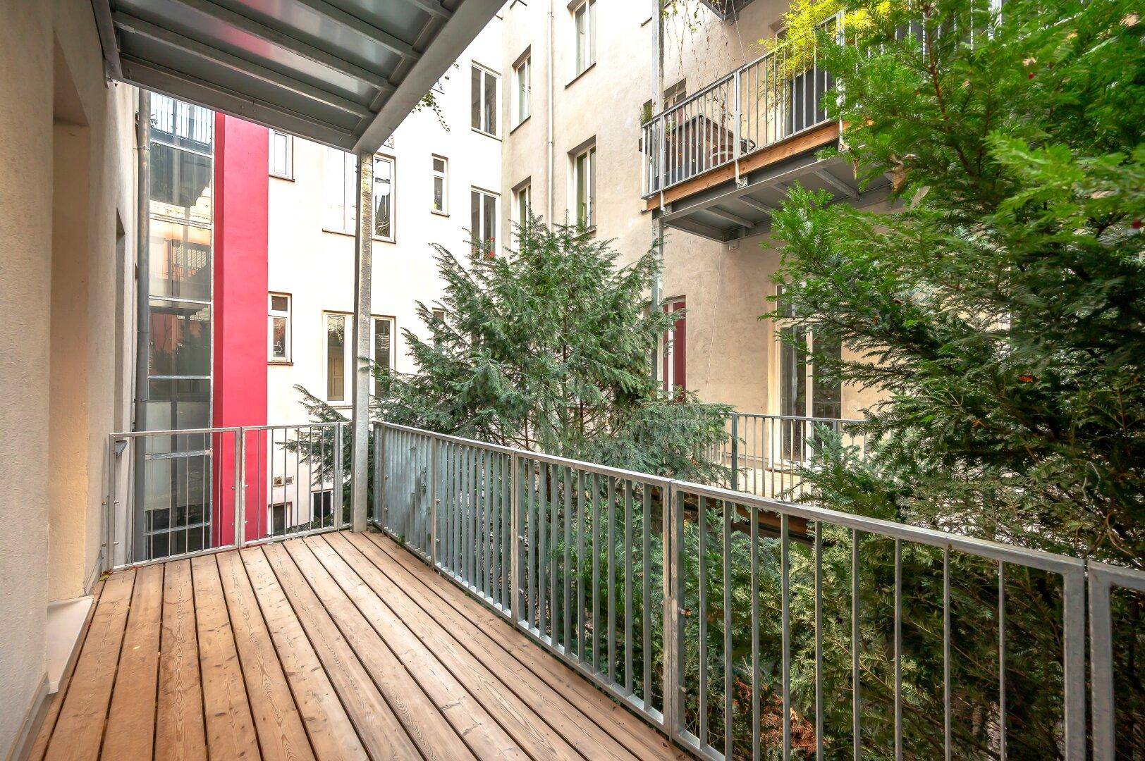 Balkon mit Holzboden und Blick auf den begrünten Innenhof und die umliegenden Gebäude.