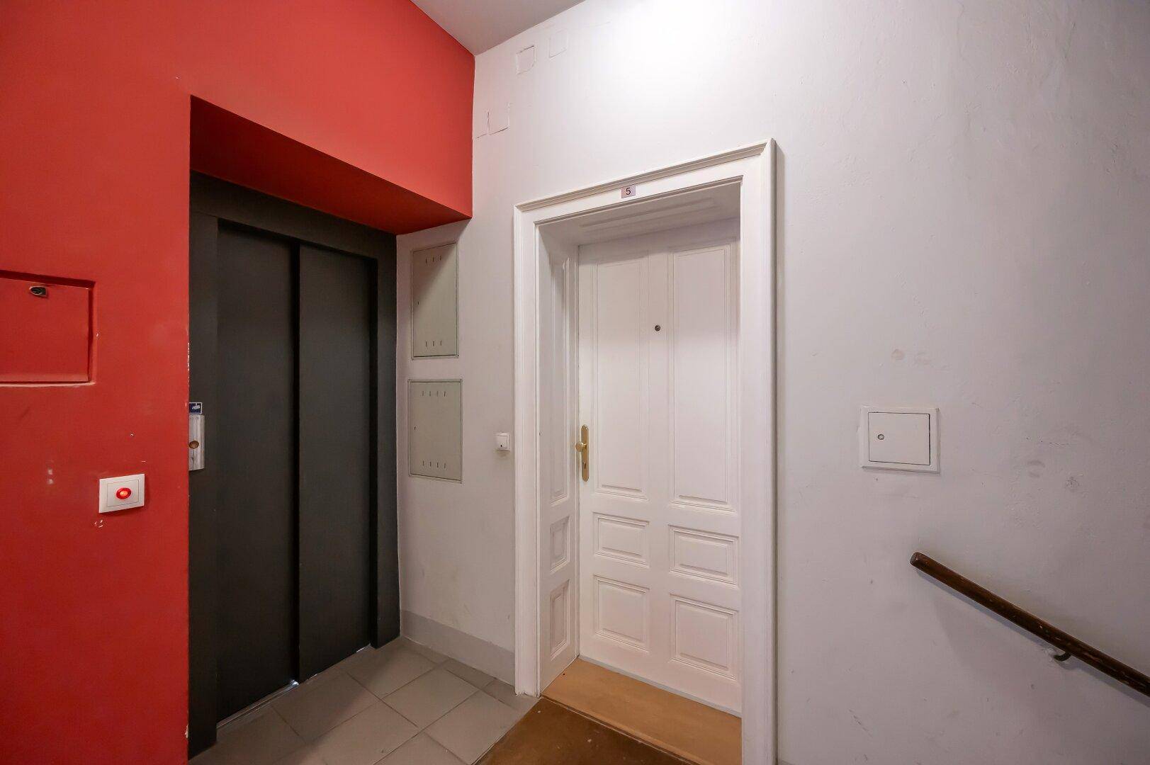 Heller Flur mit Aufzug und einer weißen Wohnungstür, die zum Eingangsbereich führt.