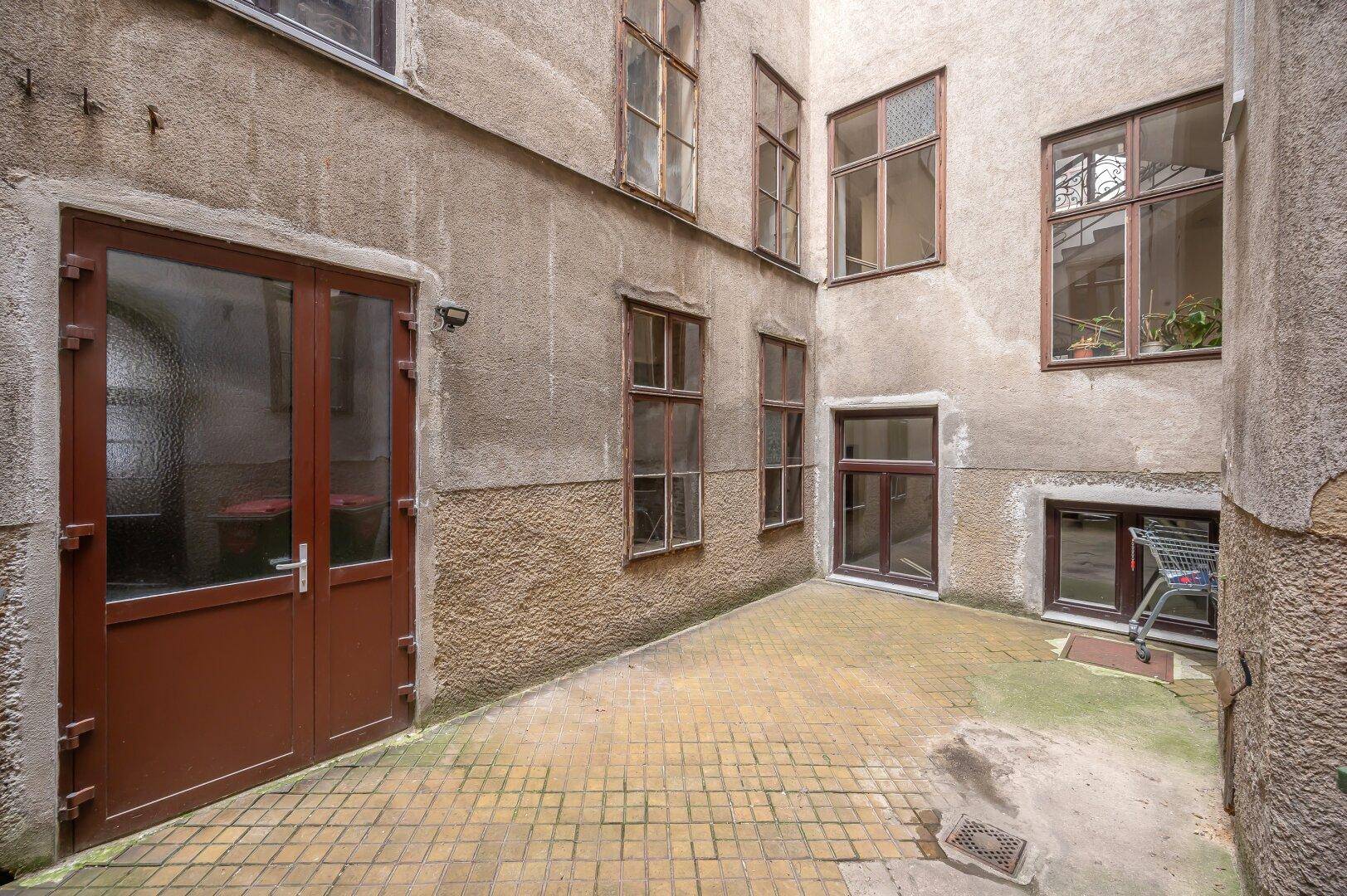 Innenhof eines Altbaus mit gepflastertem Boden und mehreren Fenstern.
