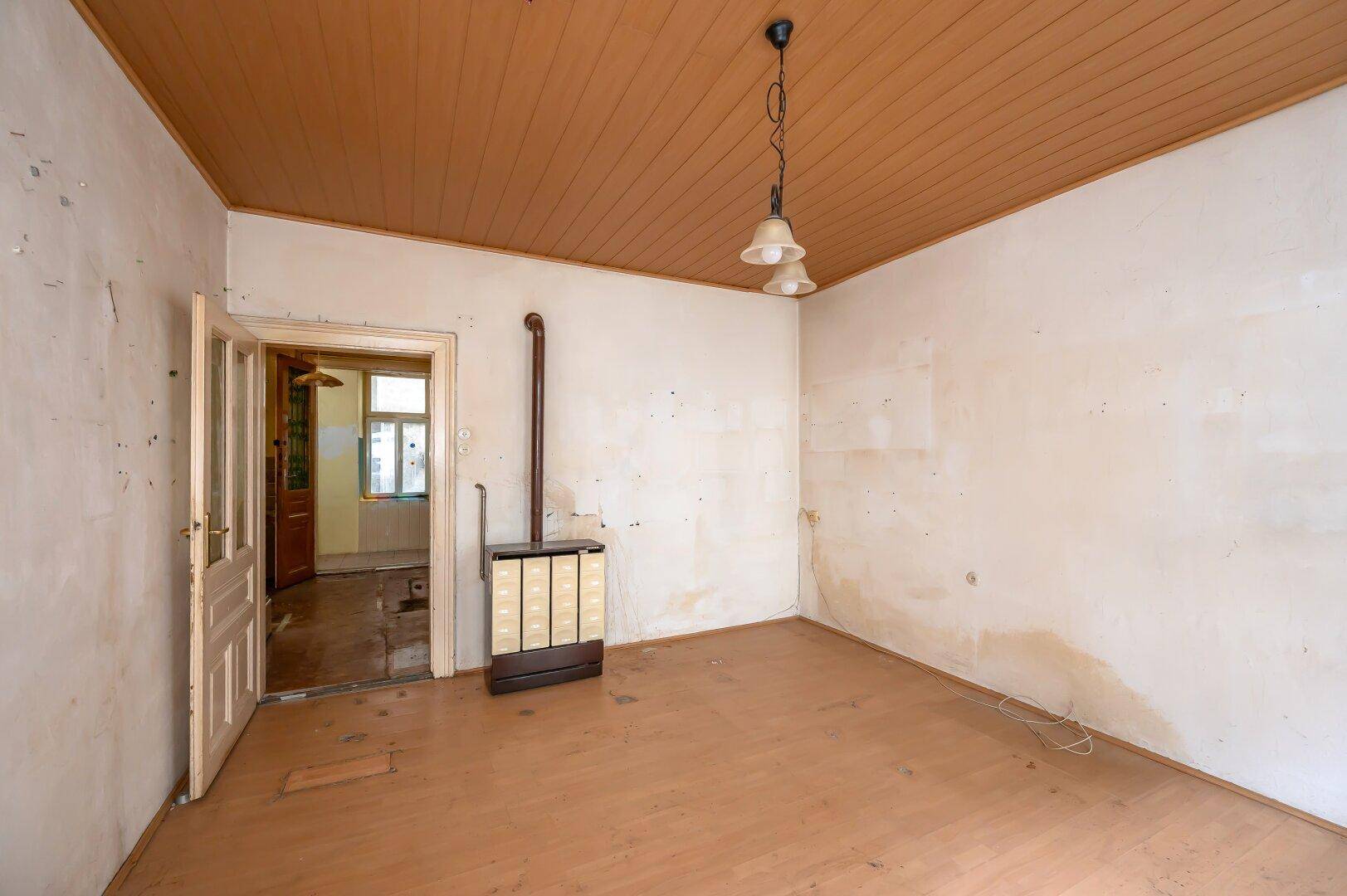 Leerer Raum mit Holzdecke, Holzboden und einem traditionellen Kachelofen.