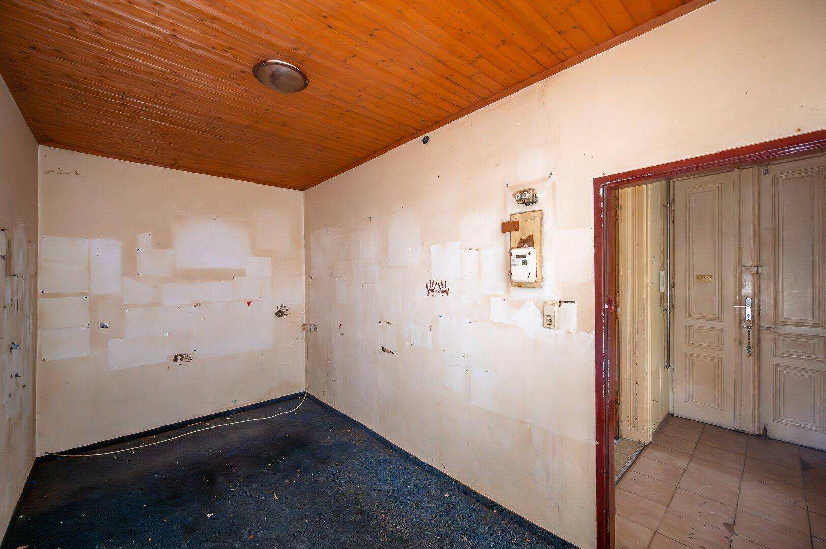 Kleiner Raum mit dunklem Teppichboden, Holzdecke und sichtbaren Elektroinstallationen.